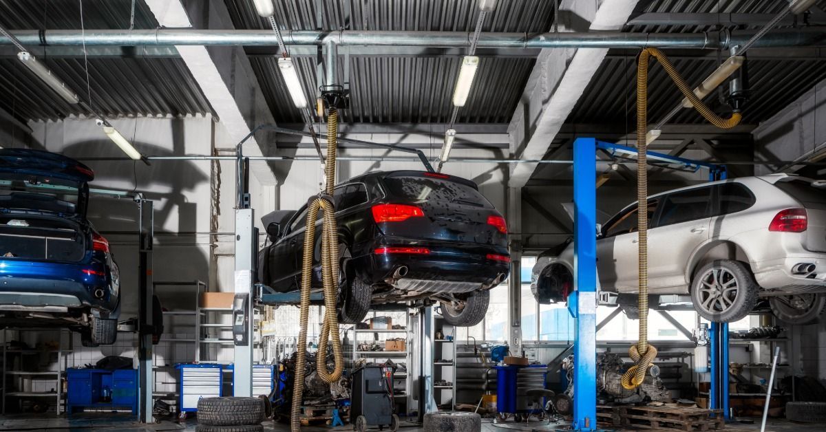 Multiple cars raised on hydraulic lifts inside an auto repair shop with equipment and tools around them.