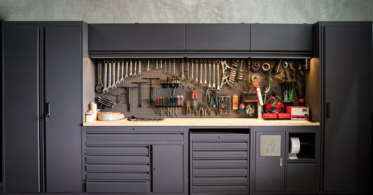 A modern garage workbench with black cabinets, pegboard tools, drawers, shelves, and a gray polished floor.