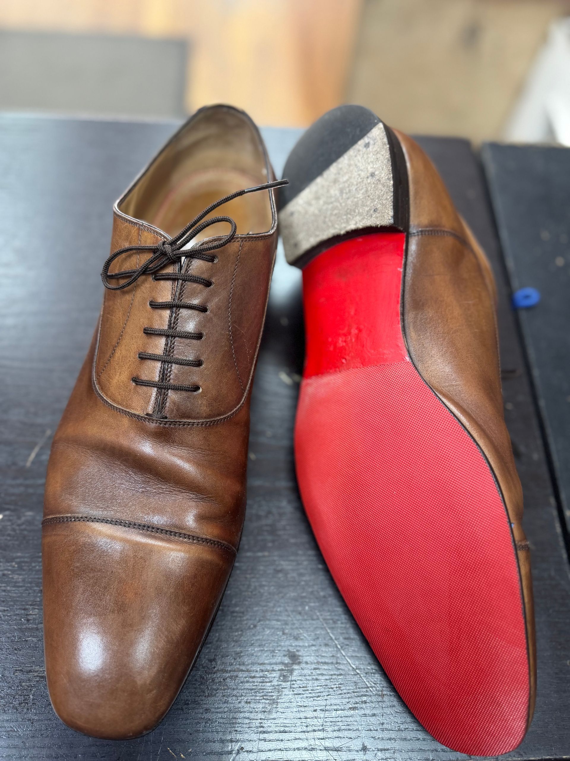 Two brown leather oxford shoes, one showing the toe and laces and the other flipped to show a bright red sole.