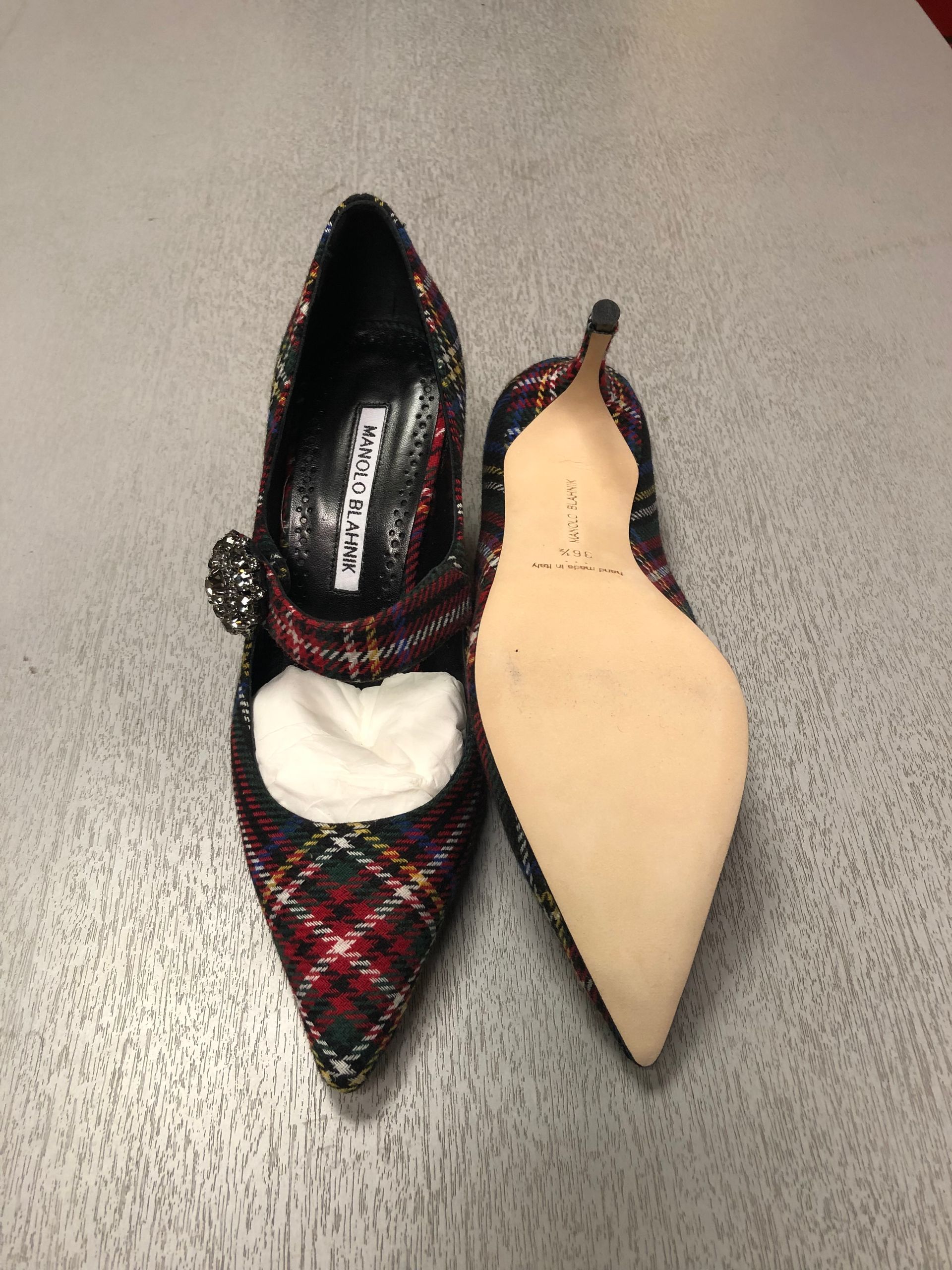 A pair of Manolo Blahnik tartan plaid pointed-toe pumps with crystal embellishments on a light gray surface.