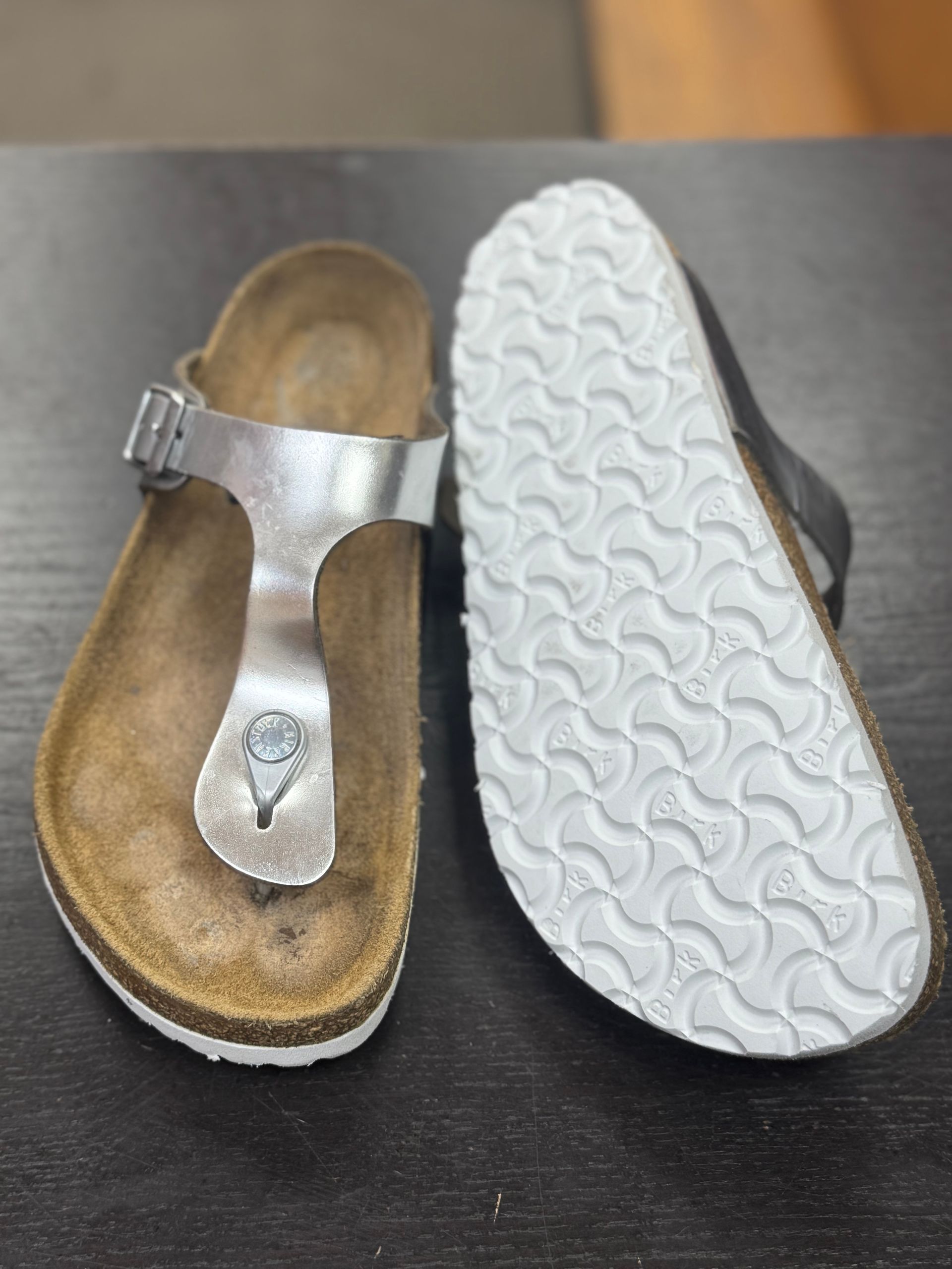 A pair of silver thong-style sandals: one showing the cork footbed and upper, the other showing the white treaded sole.