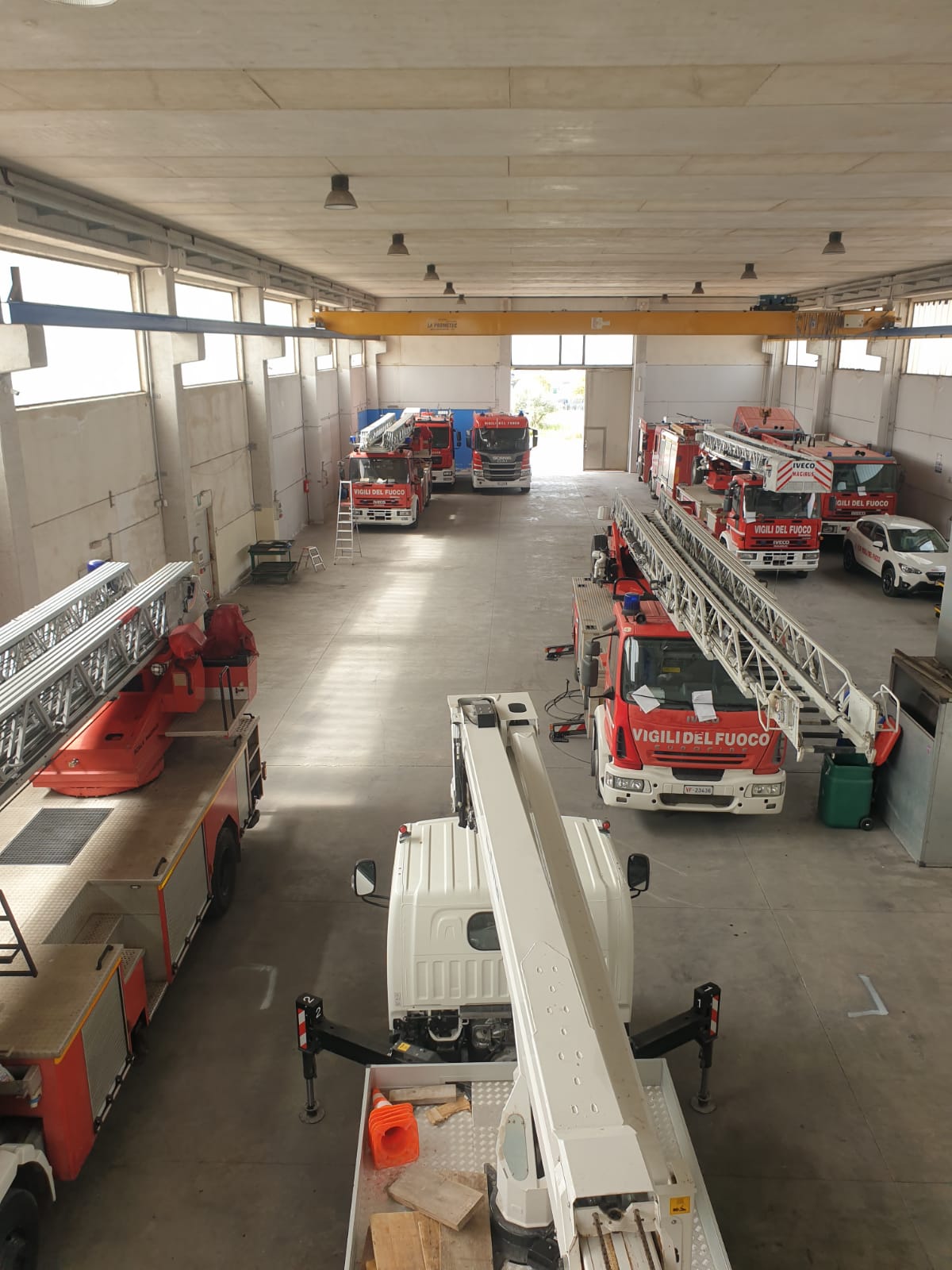 Interno della stazione dei pompieri, diversi camion dei pompieri rossi parcheggiati all'interno di un ampio piazzale.