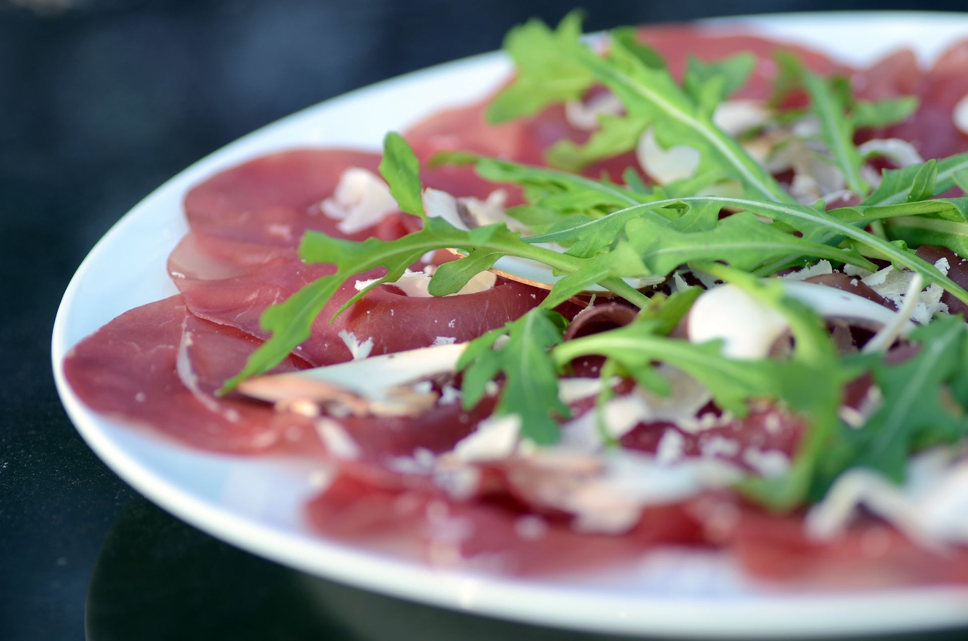 Teller mit dünn geschnittenem Wurstfleisch, garniert mit Rucola und geriebenem Käse.