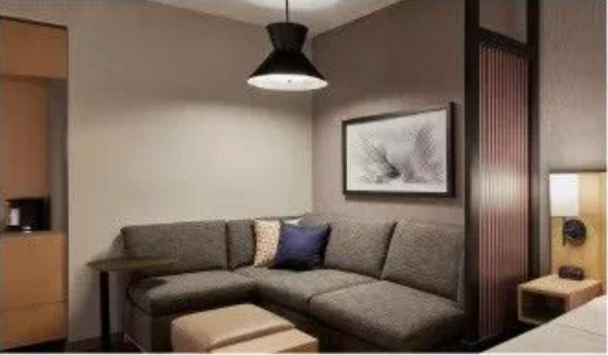 An artist 's impression of a hotel room with a couch and ottoman.