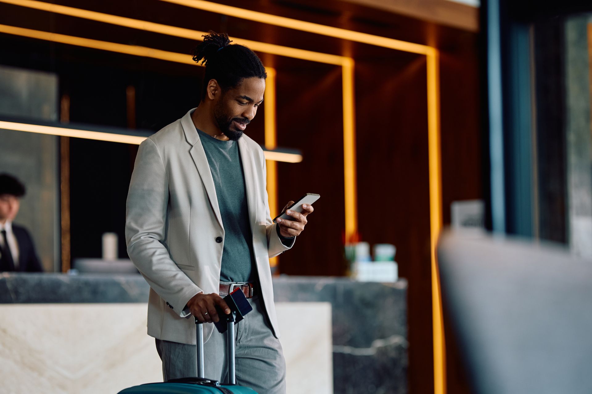 A man with a suitcase is looking at his cell phone in a hotel lobby.
