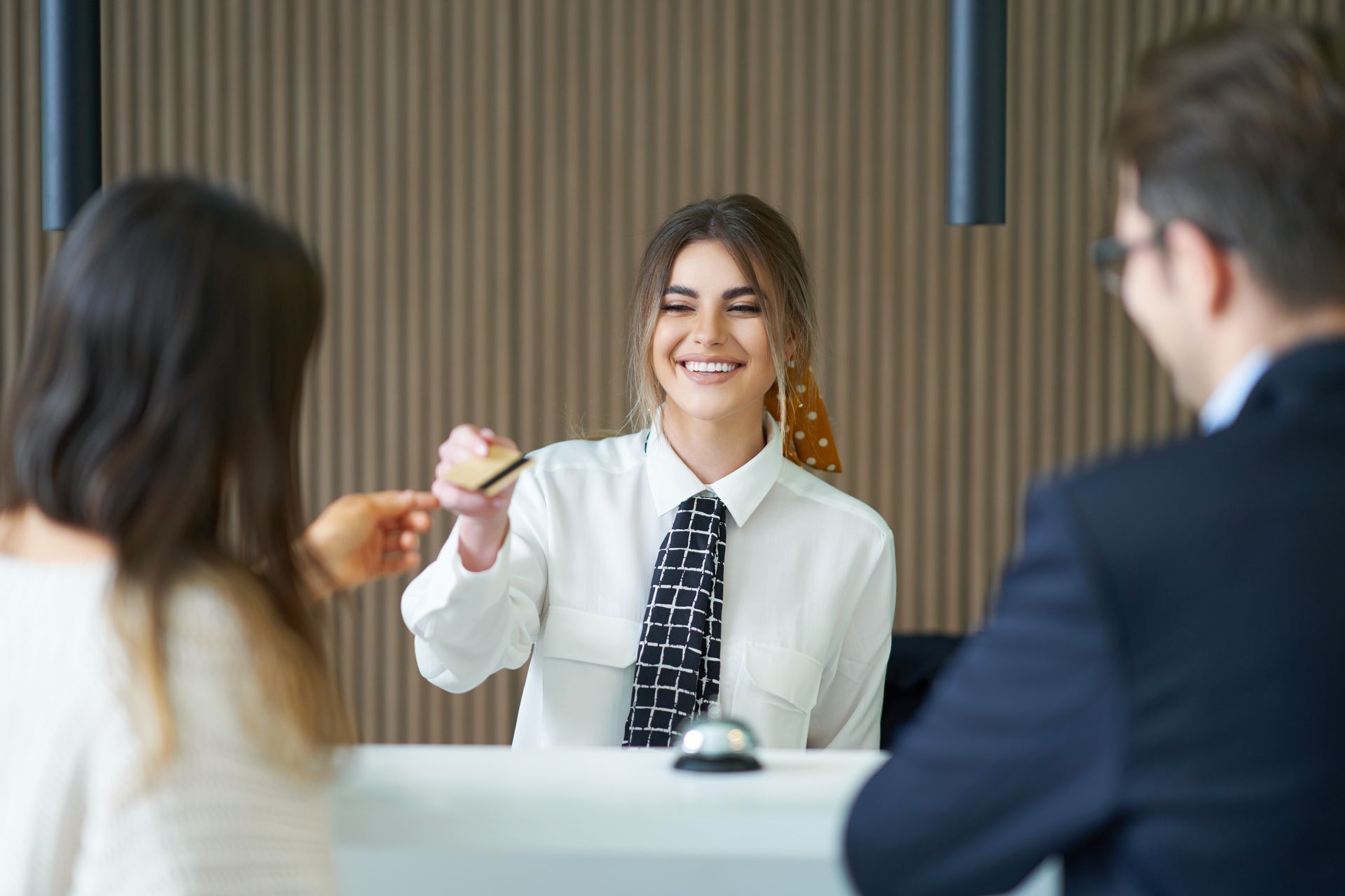 A woman is giving a credit card to a man at a hotel reception.