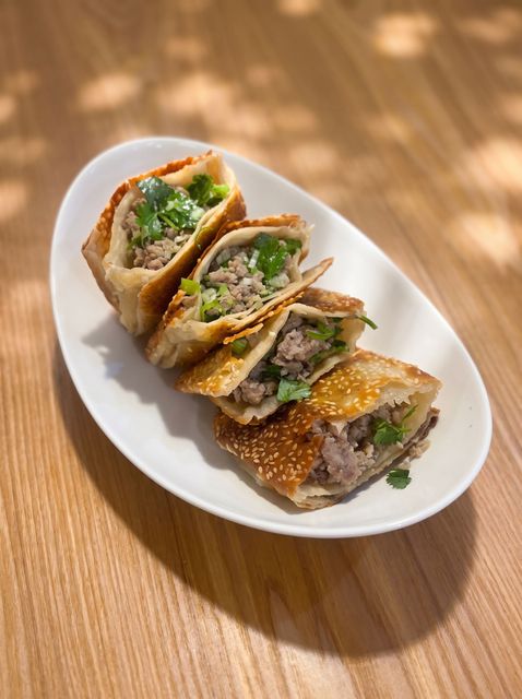 Sliced savory rolls with meat and greens on a white plate on a wooden table