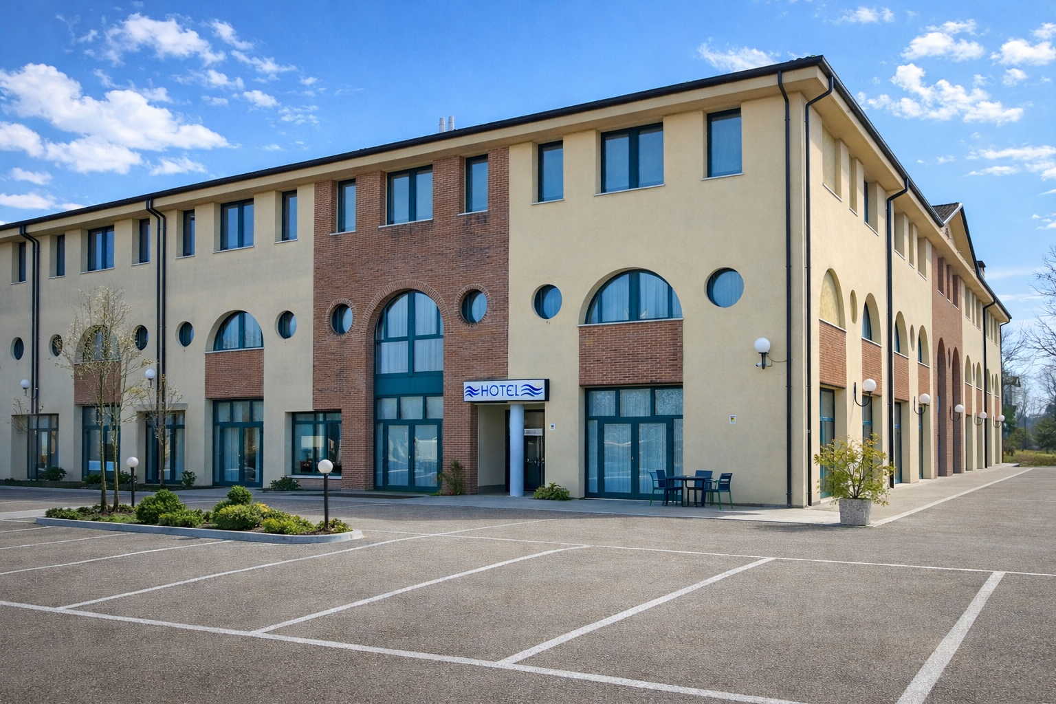 Edificio dell'hotel con auto parcheggiate di fronte. Esterno in mattoni color crema e rosso.