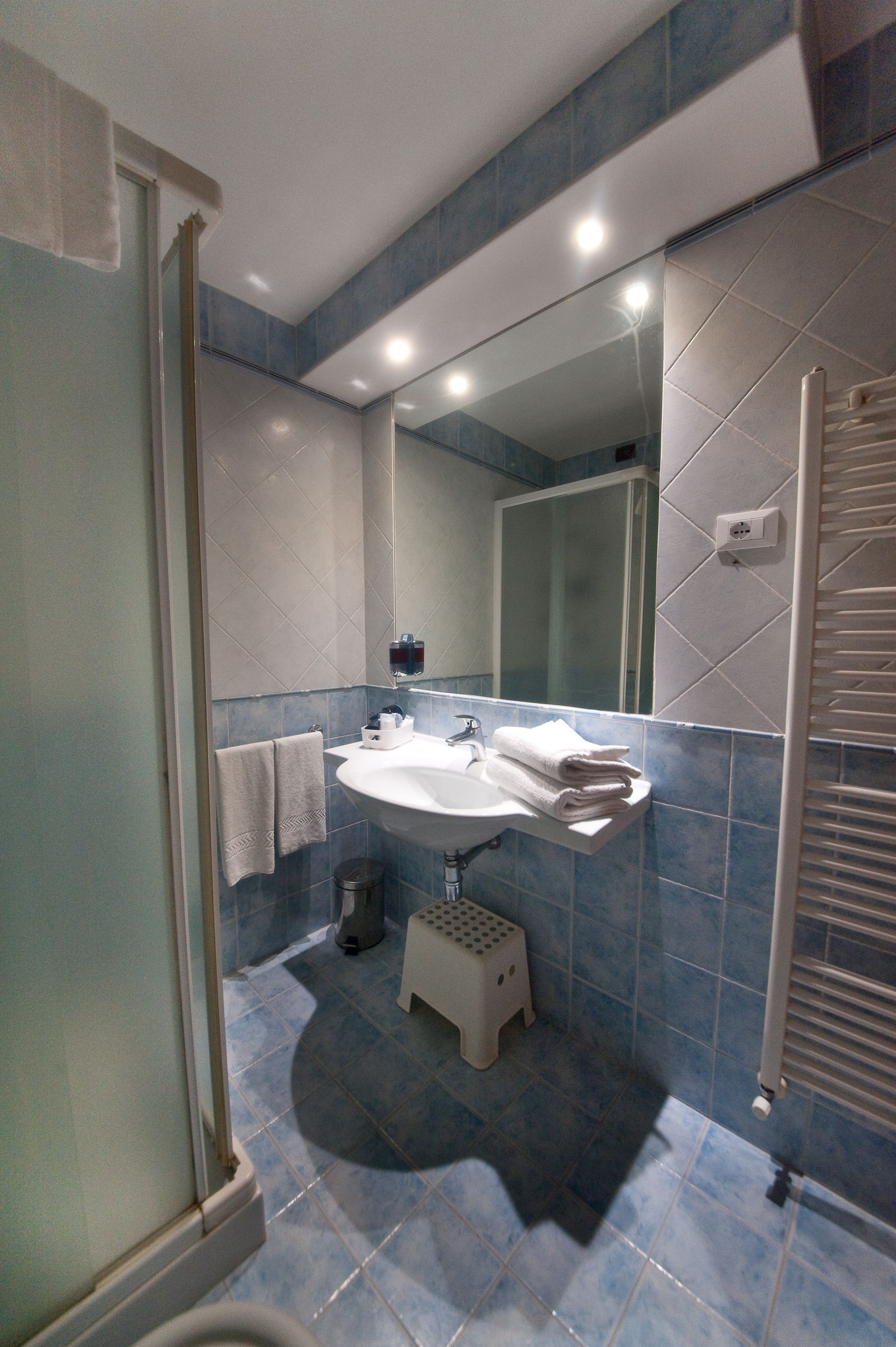 Bagno con pareti piastrellate blu, lavandino, doccia e portasciugamani.