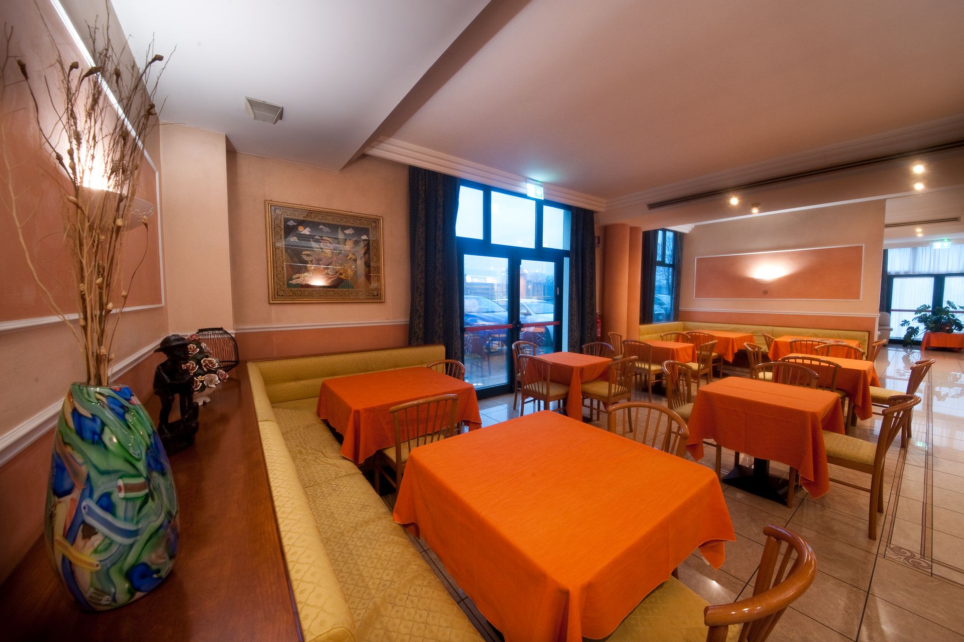 Interno del ristorante con tovaglie arancioni, pareti neutre e uno scorcio dell'esterno.