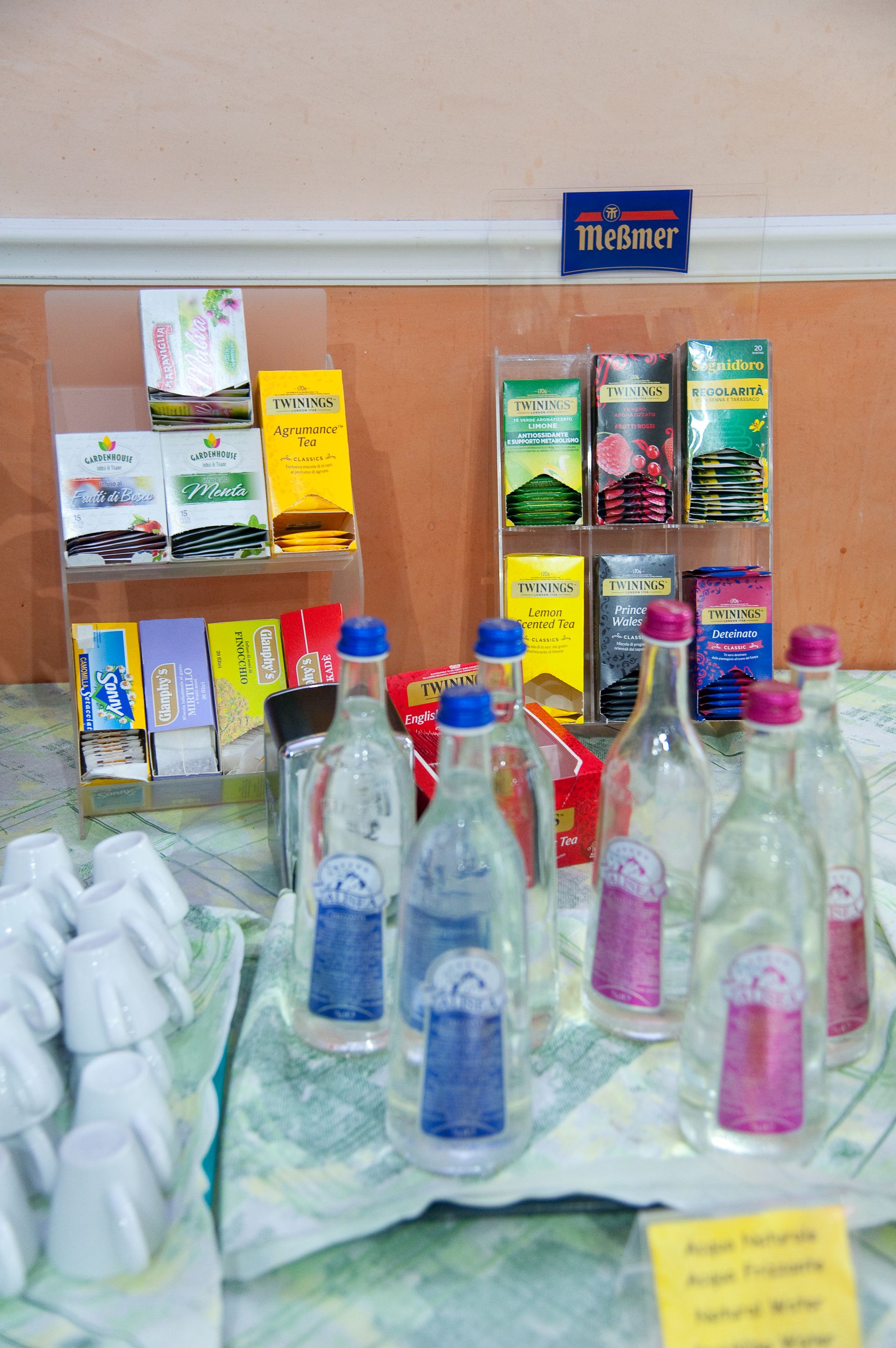 Bottiglie d'acqua con etichette blu e rosa esposte insieme ad altri prodotti confezionati.