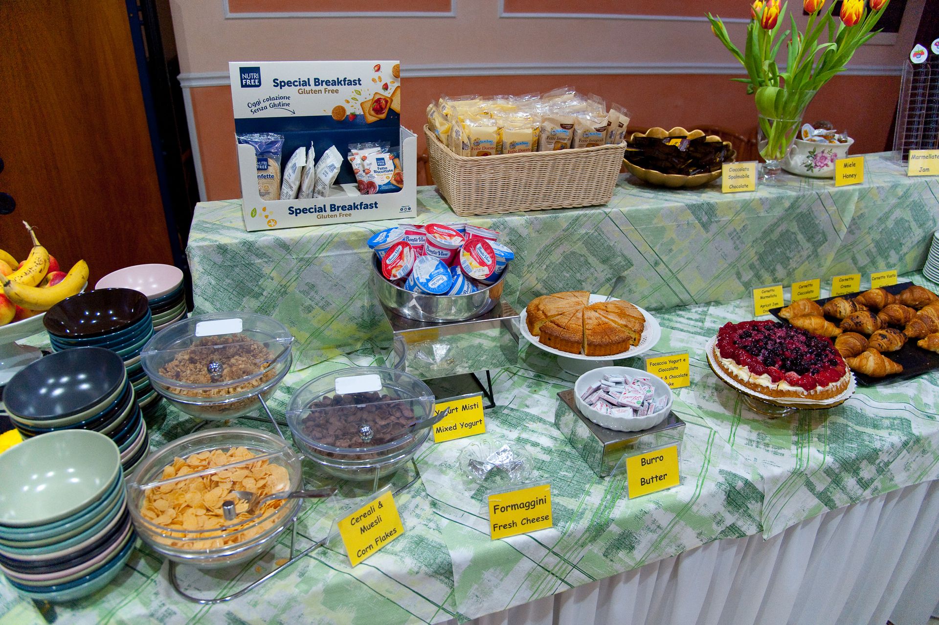 Tavolo per la colazione a buffet con cereali, pasticcini, frutta e fiori.