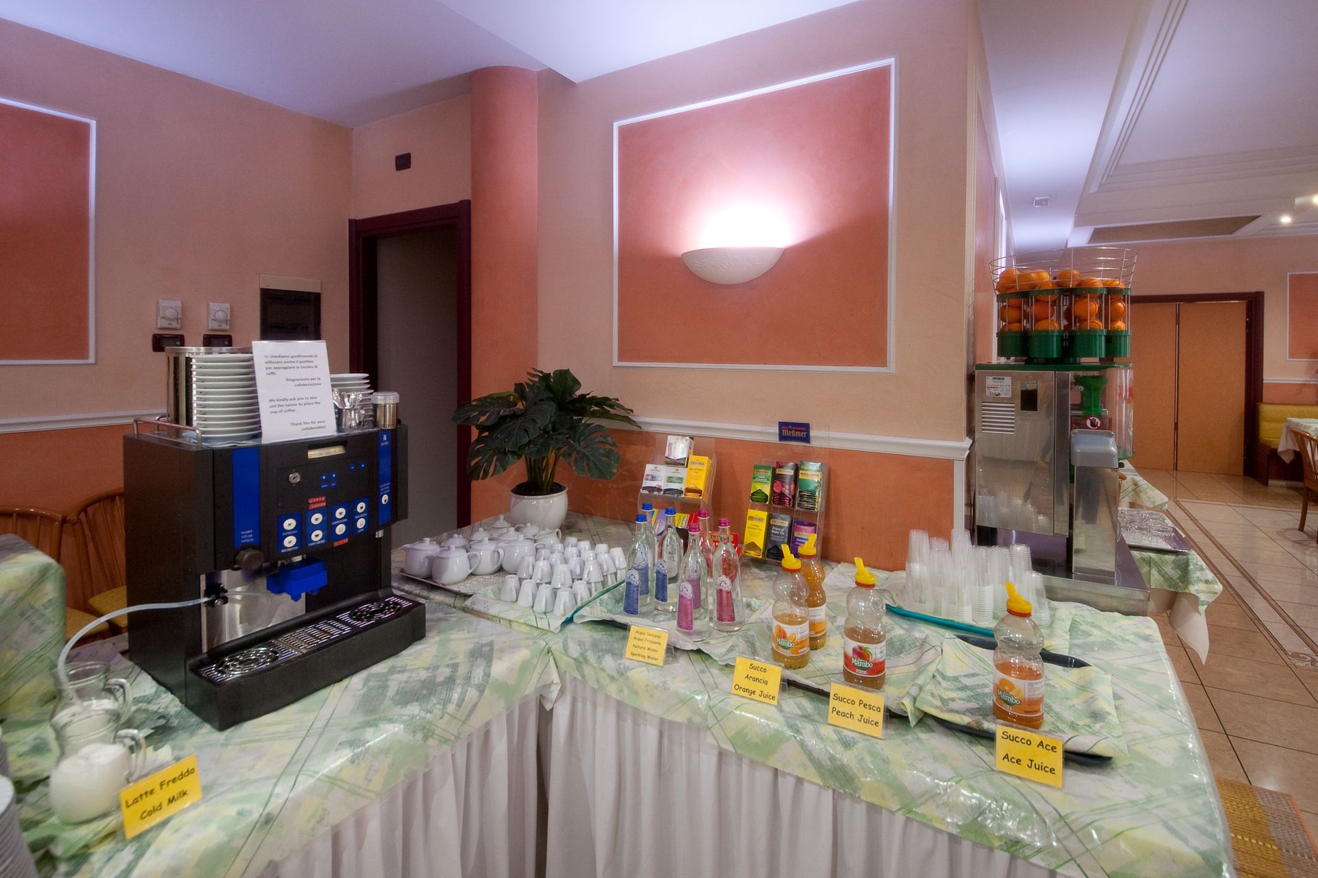 Colazione a buffet in hotel con macchina per il caffè, distributori di succhi, bicchieri e bevande in bottiglia.