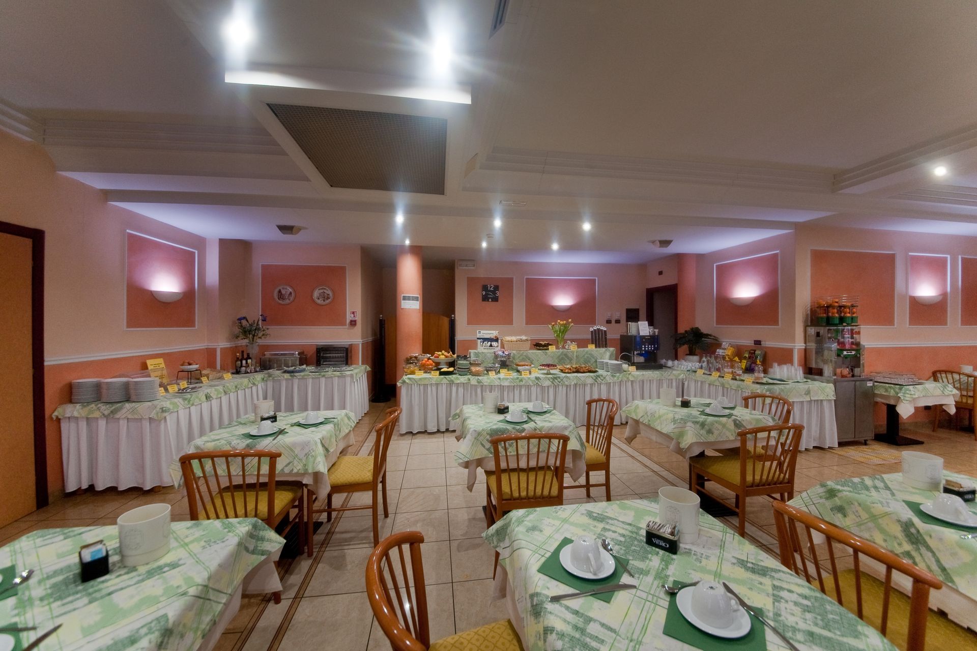 Sala da pranzo dell'hotel con tavoli, sedie, buffet di cibo e illuminazione dall'alto.
