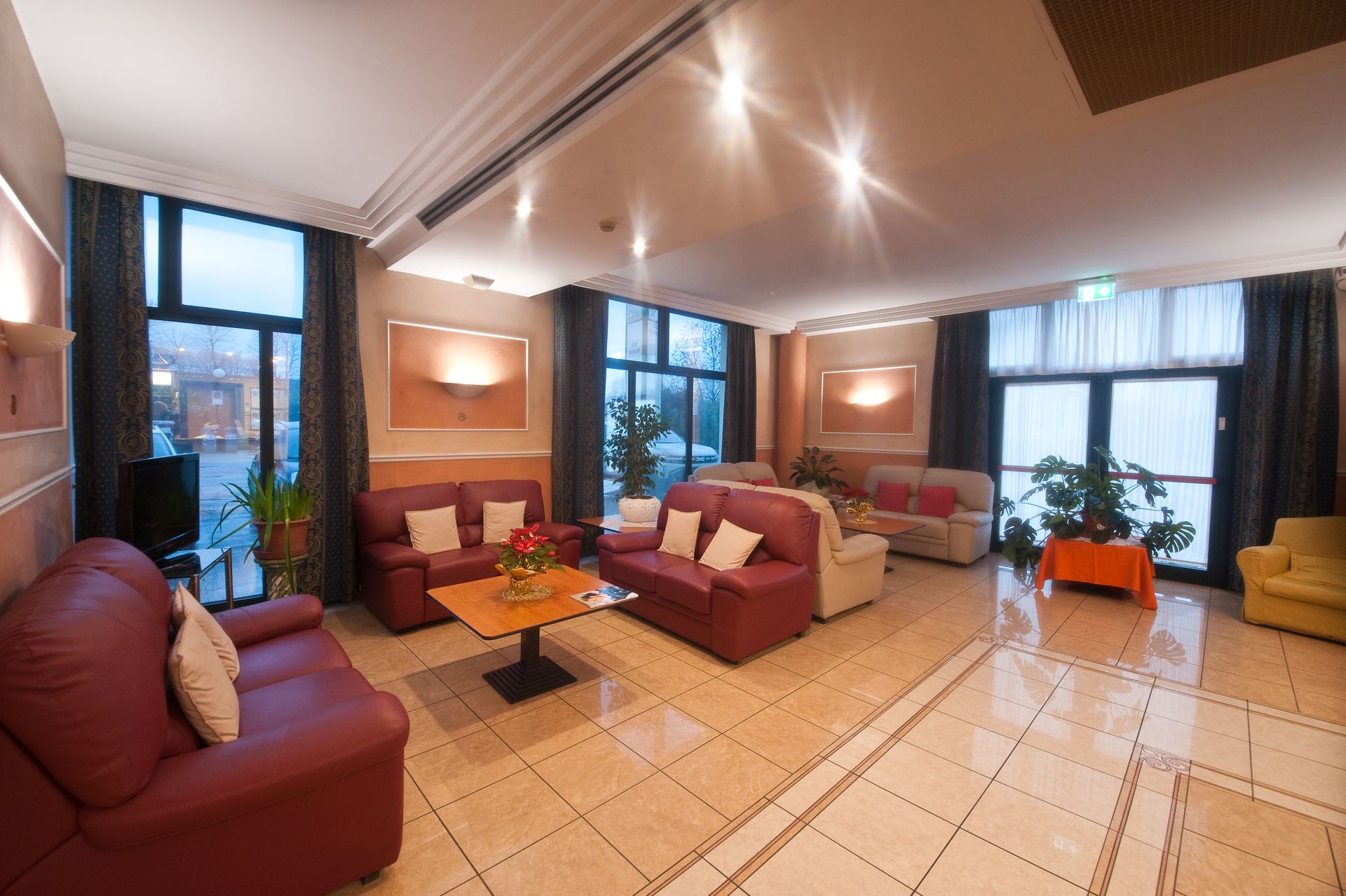 Hall dell'hotel con divani rossi e beige, tavolini da caffè e ampie finestre.