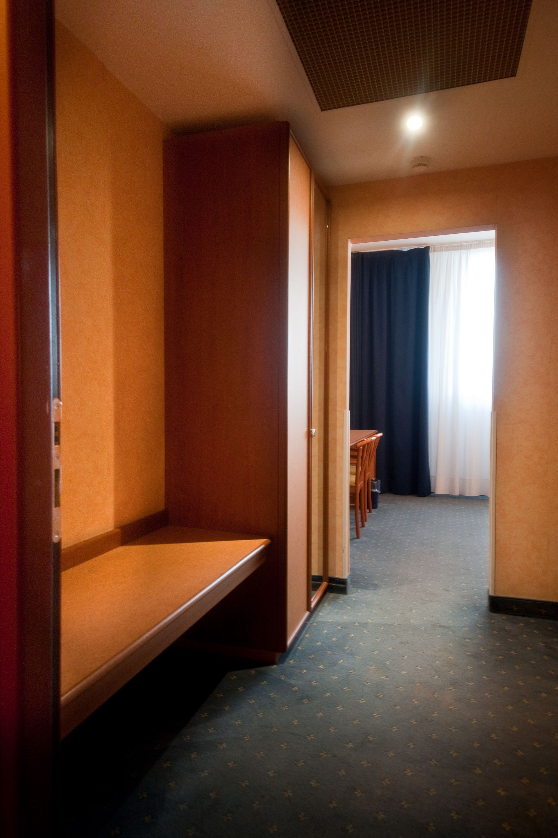 Corridoio con scrivania incorporata, che conduce a una stanza con tende e tavolo. Moquette scura, pareti arancioni.