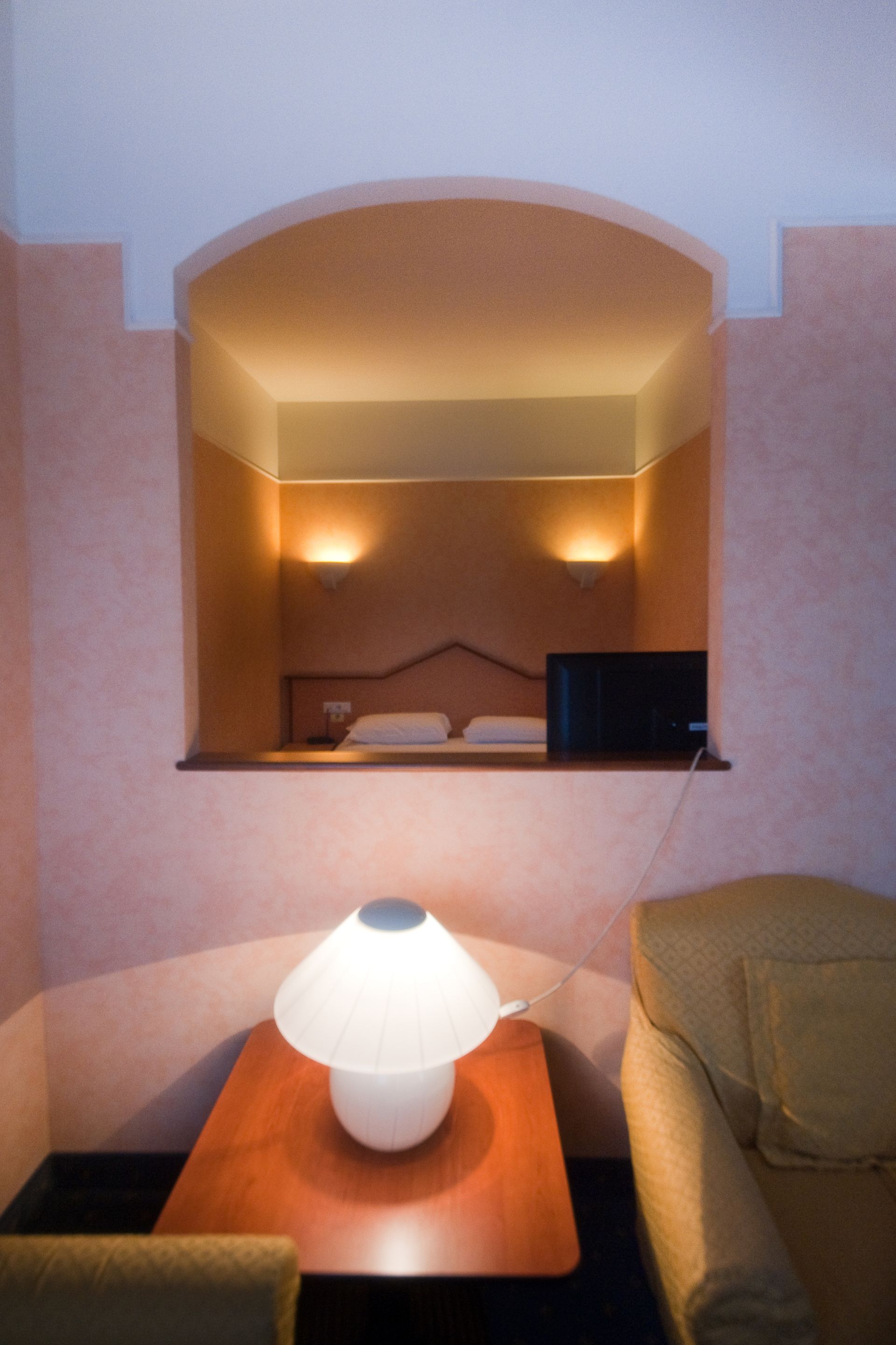 Un letto e una TV sono incassati in una parete. Una lampada e un divano sono posizionati di fronte all'alcova.