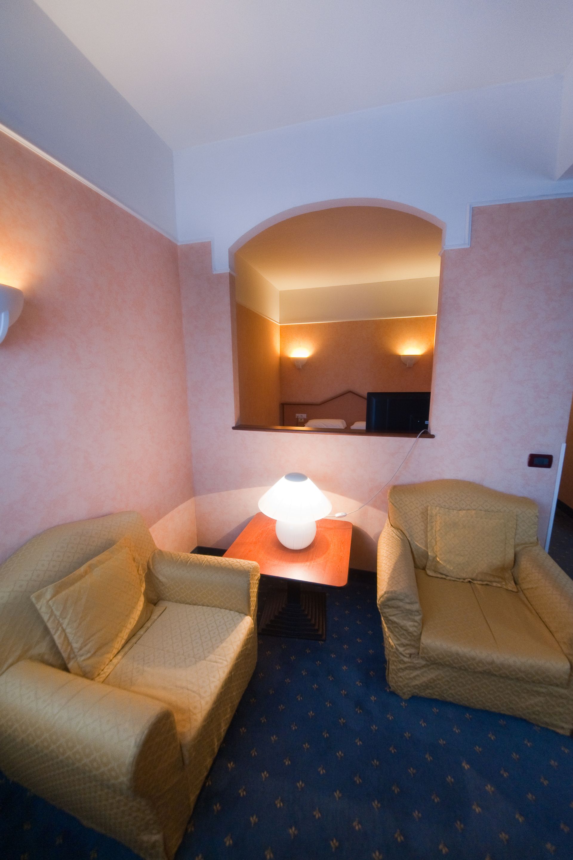 Due poltrone gialle sono disposte una di fronte all'altra, vicino a un tavolino con lampada, in una nicchia color pesca.