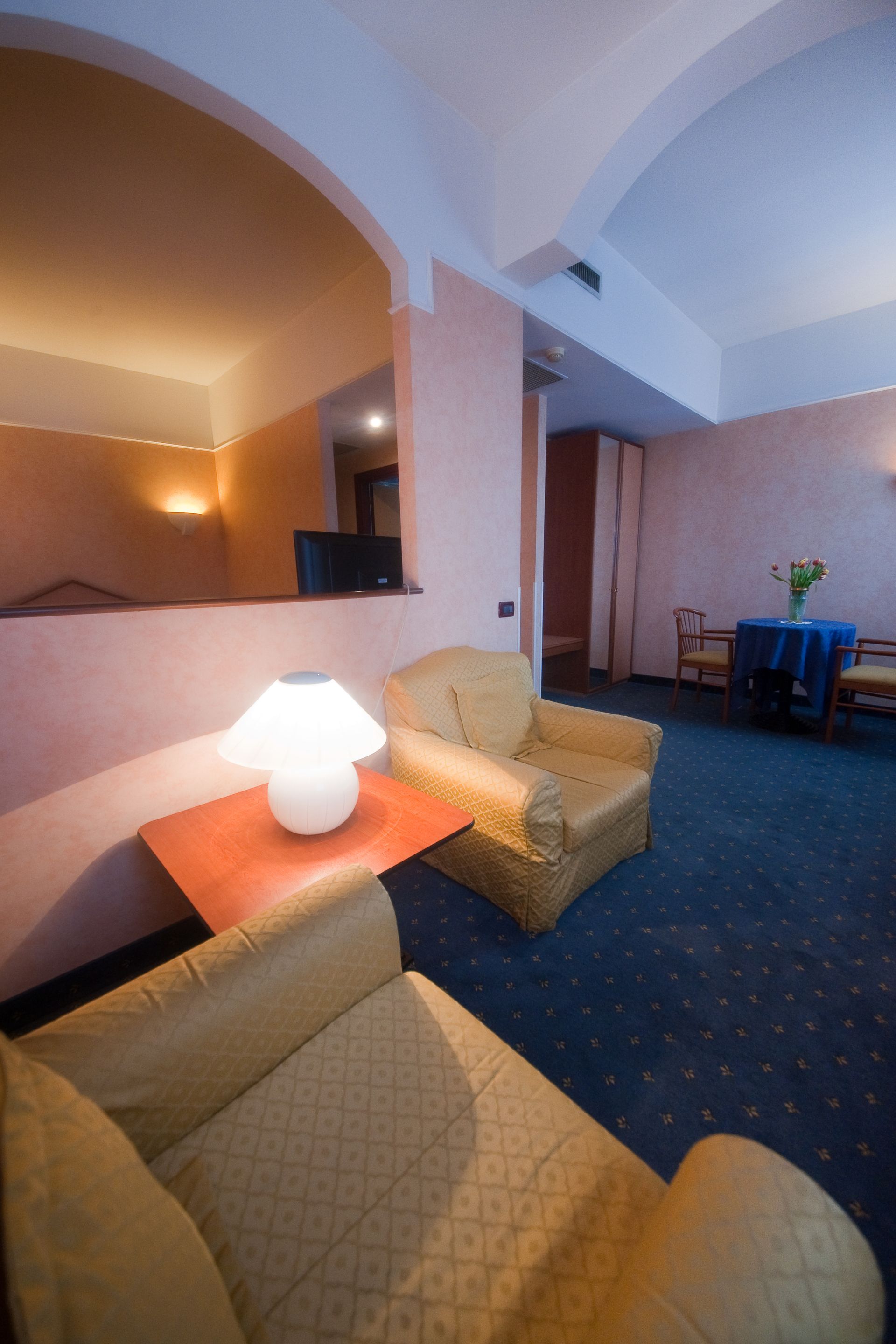 Accogliente zona soggiorno dell'hotel con due poltrone, lampada sul tavolino e un piccolo tavolo da pranzo sullo sfondo.