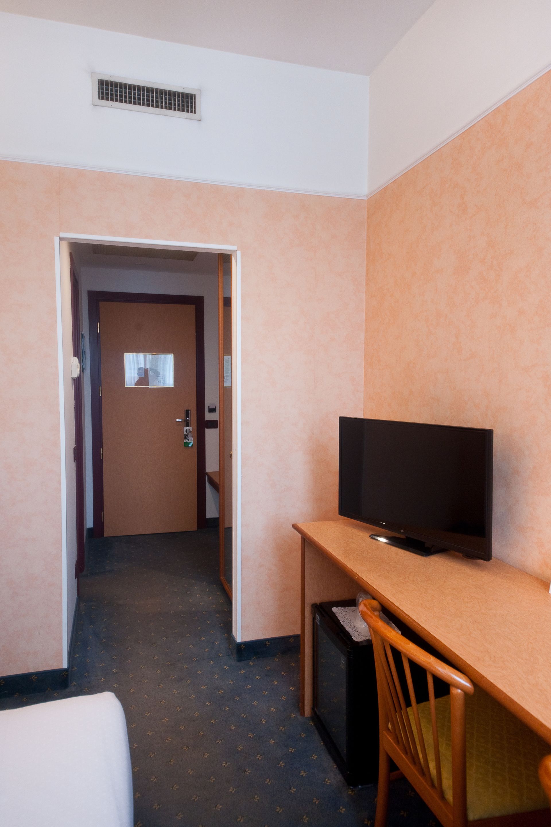 Interno di una camera d'albergo con scrivania, TV e porta aperta che conduce a un'altra stanza.