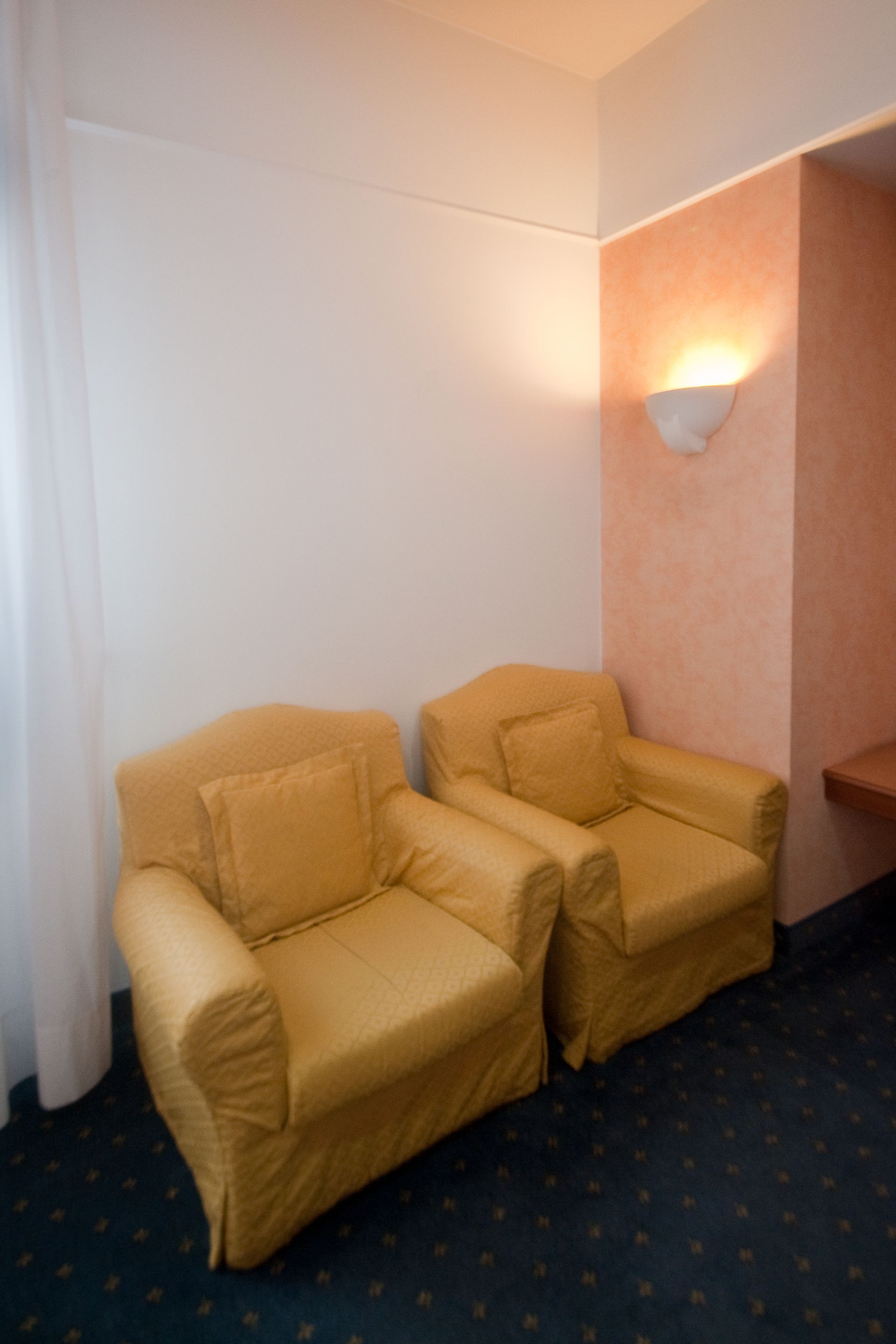 Due poltrone gialle si trovano in un angolo di una stanza con pareti bianche e color pesca.