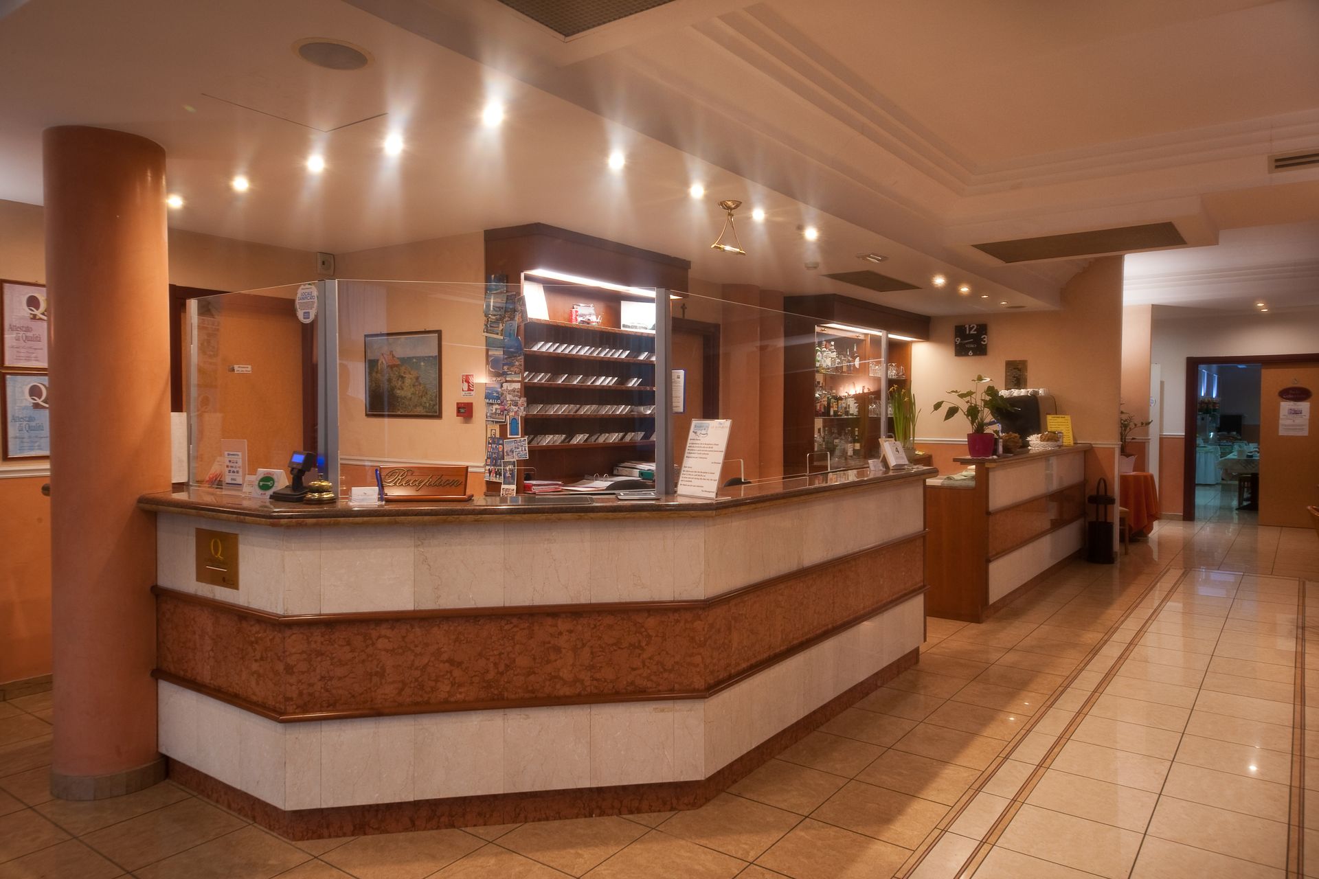 Reception dell'hotel con bancone marrone e bianco, illuminato da luci soffuse.