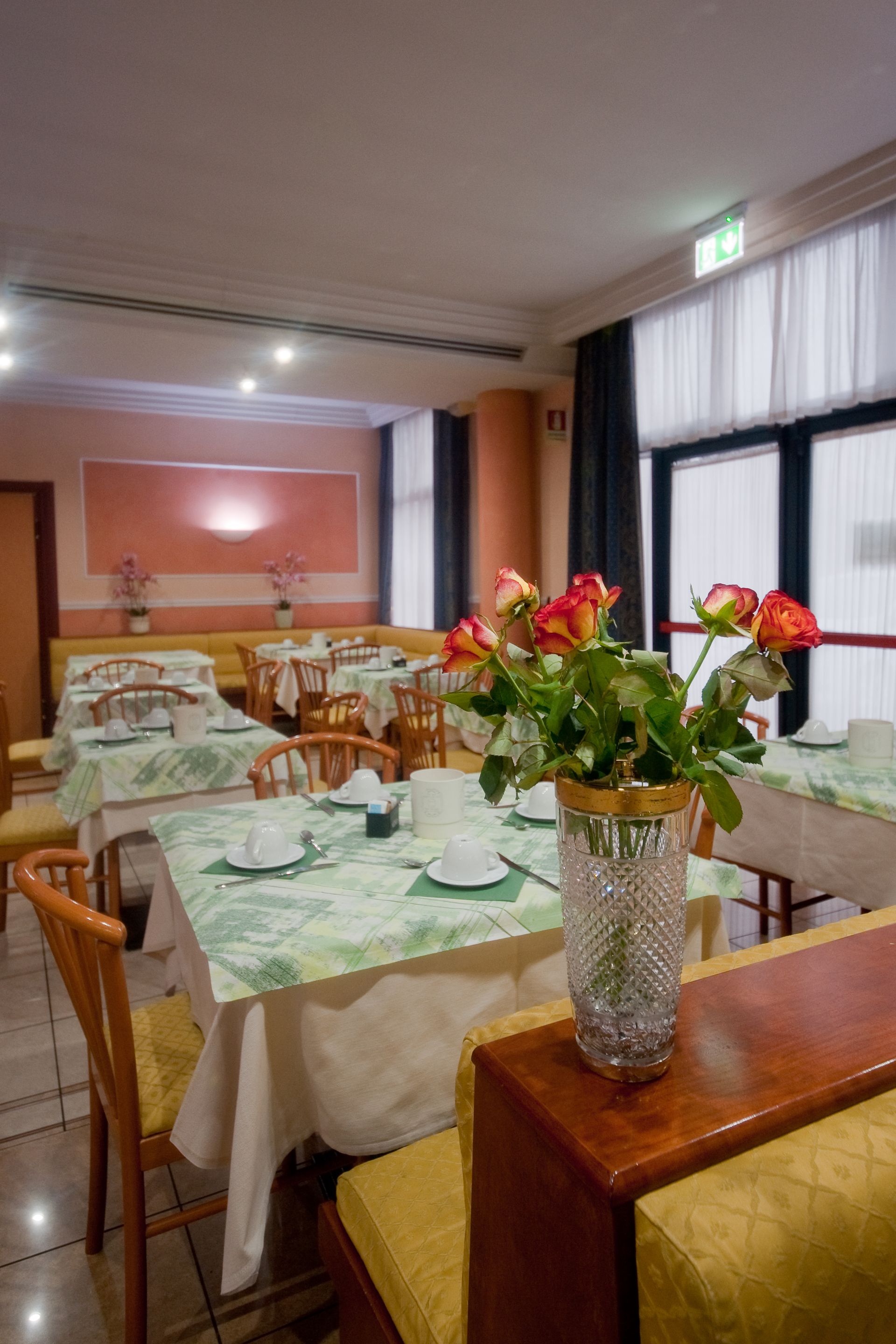 Sala da pranzo del ristorante con tavoli apparecchiati per un pasto; bouquet di rose su un tavolo di legno.