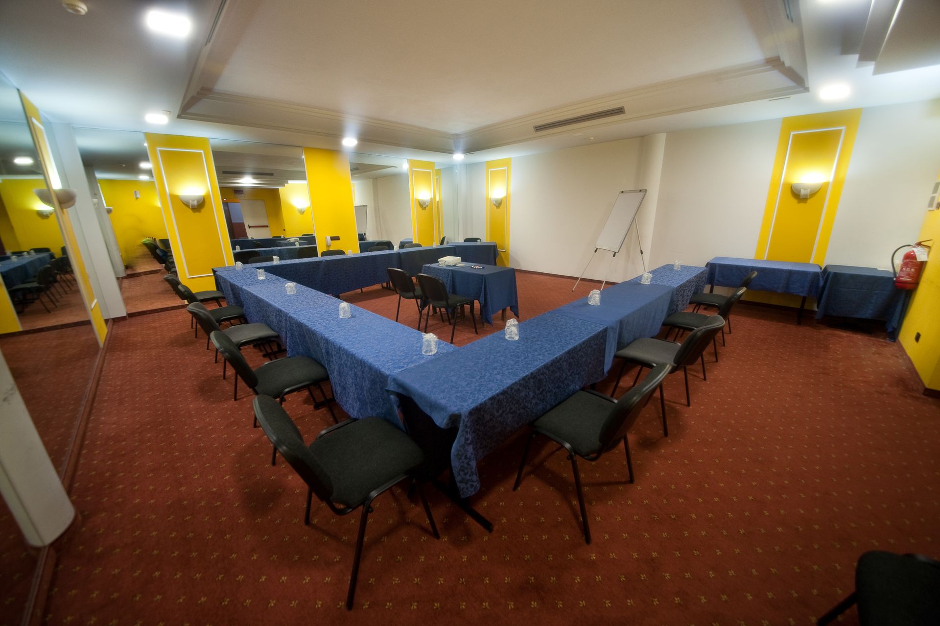 Sala conferenze allestita con tavoli a U, sedie nere e pareti gialle e bianche.