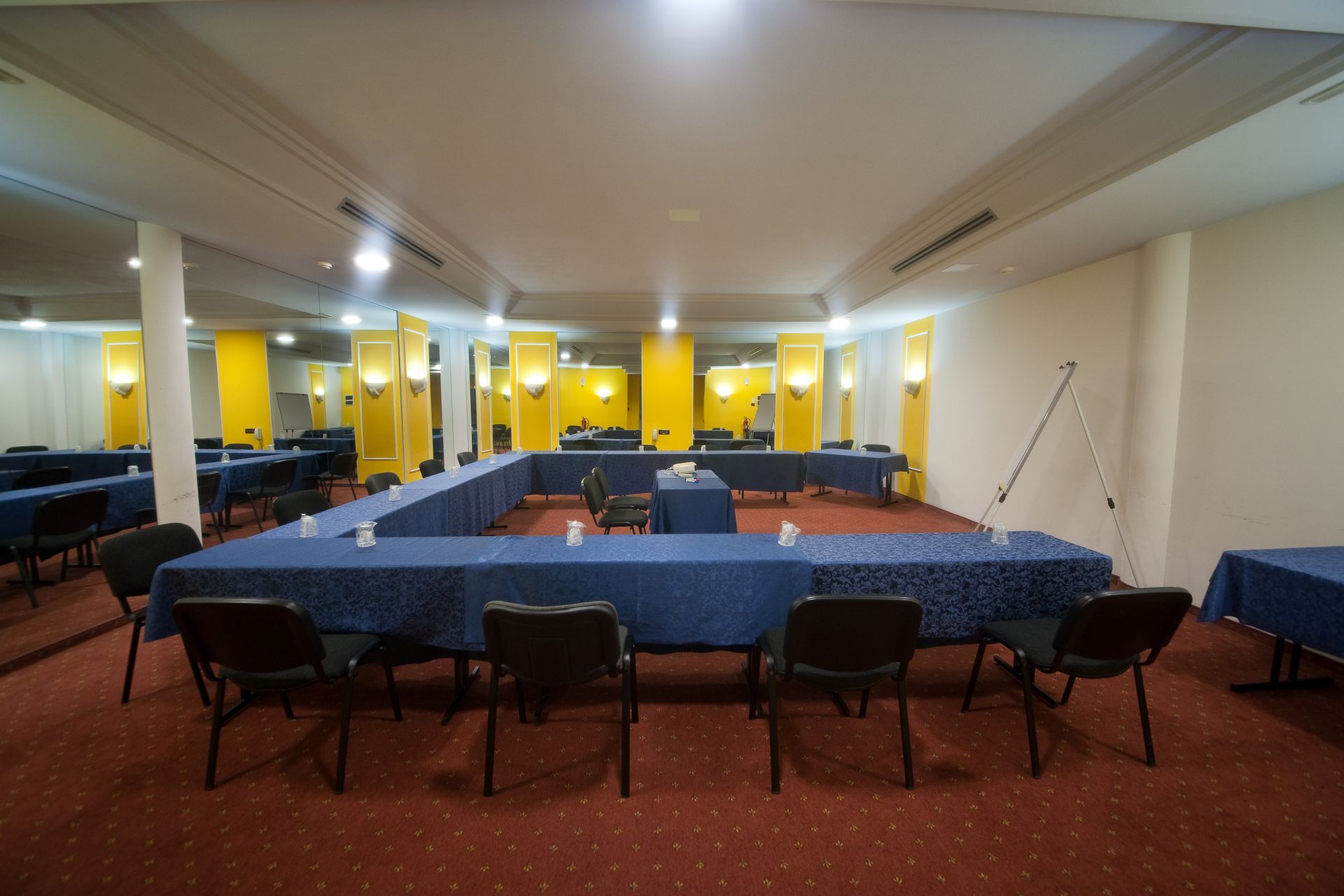 Sala conferenze con tovaglie blu, sedie nere e colonne gialle.