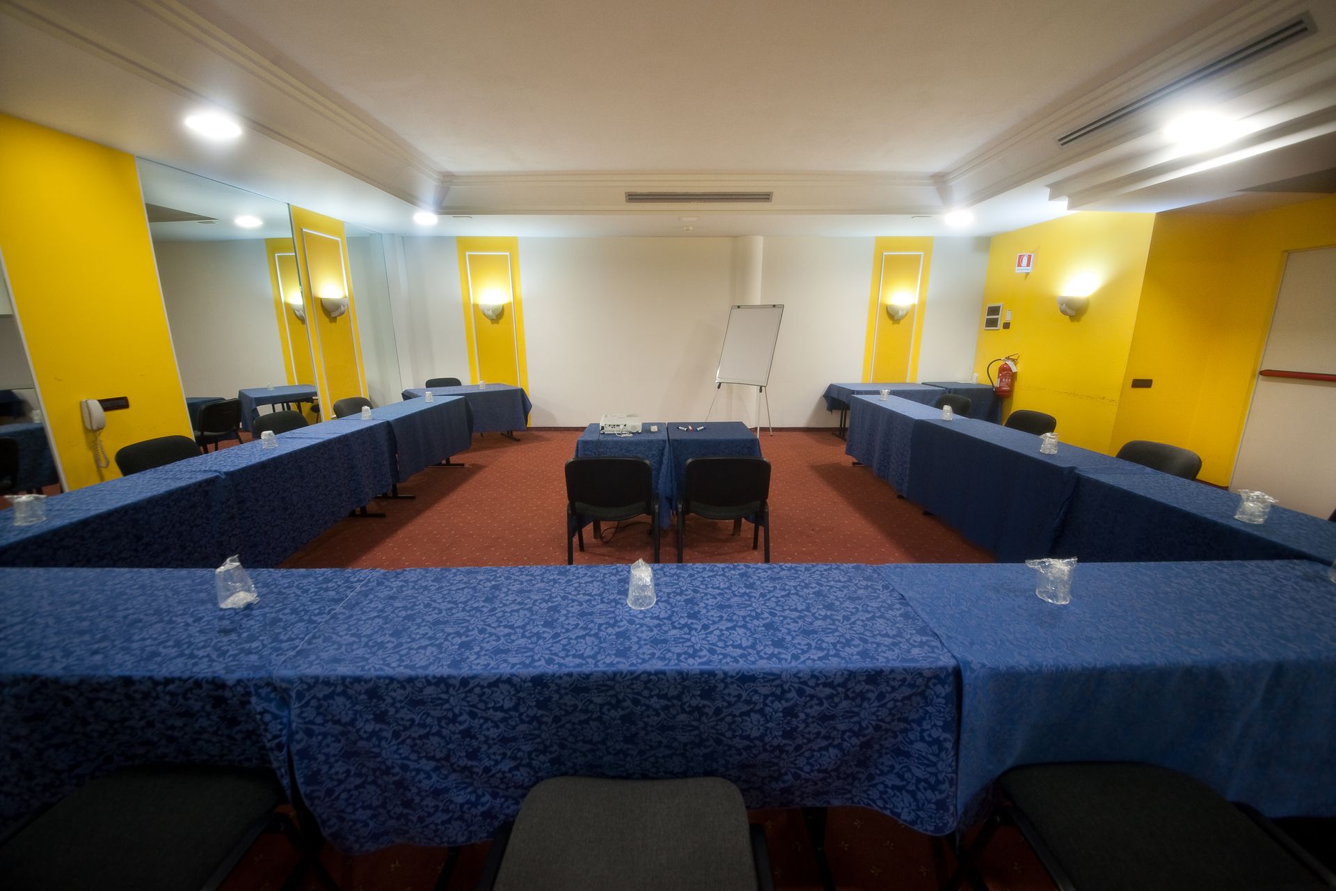 Sala conferenze con tavoli blu disposti a U, dettagli gialli e una lavagna bianca.