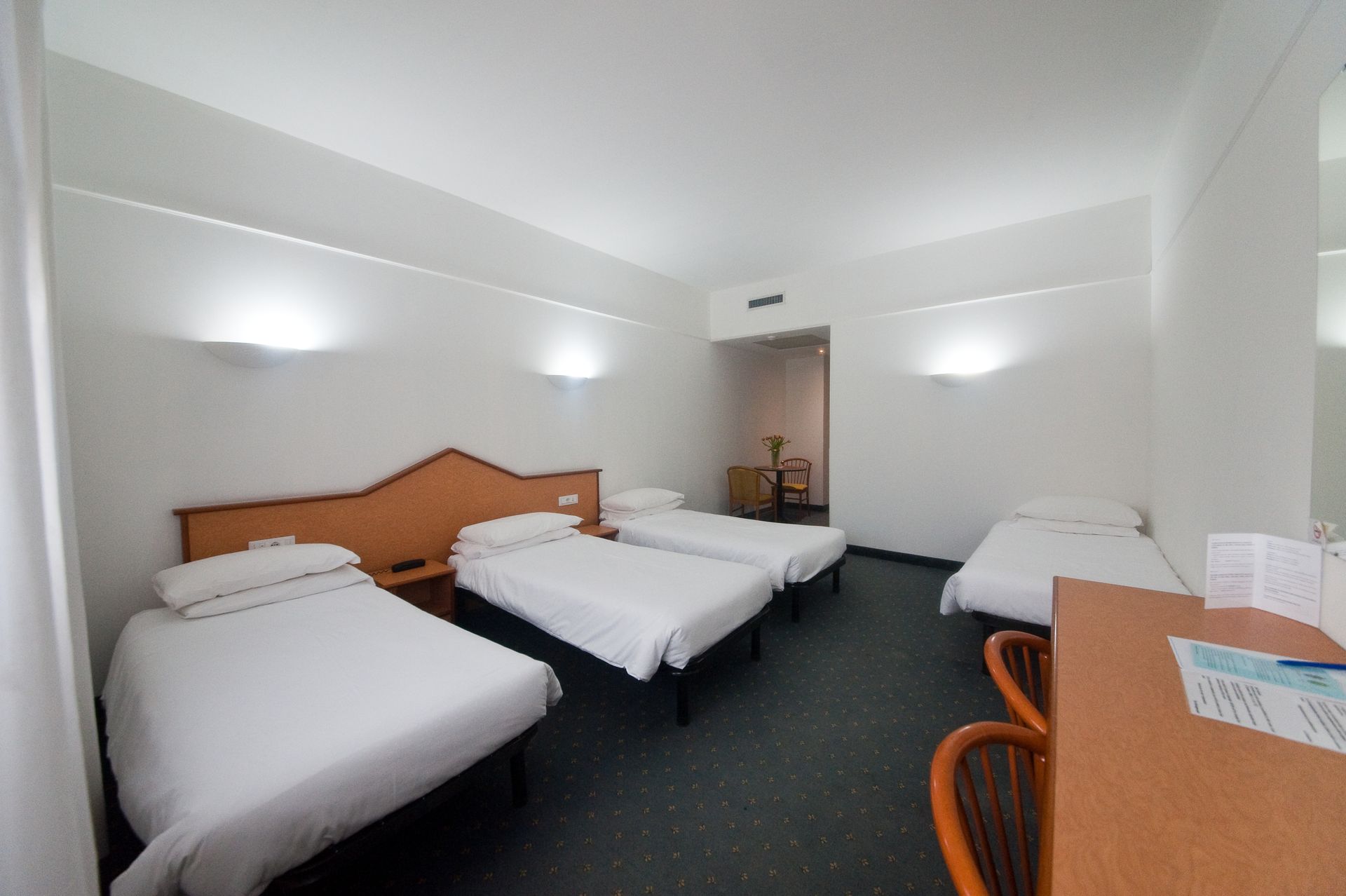 Camera d'albergo con quattro letti, una scrivania e un arredamento minimalista.