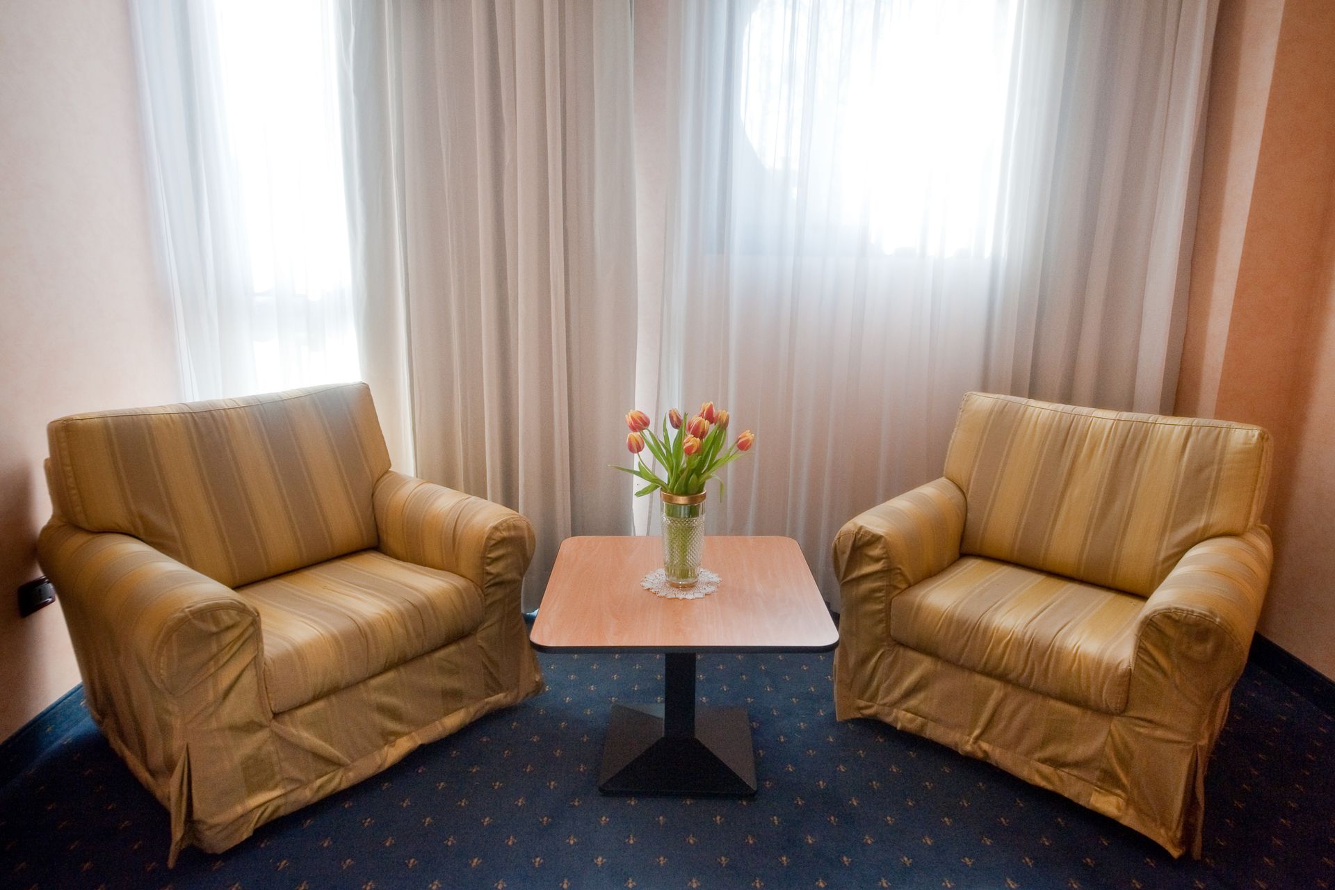 Due poltrone imbottite sono di fronte a un tavolino con fiori, di fronte a una finestra con tende bianche.