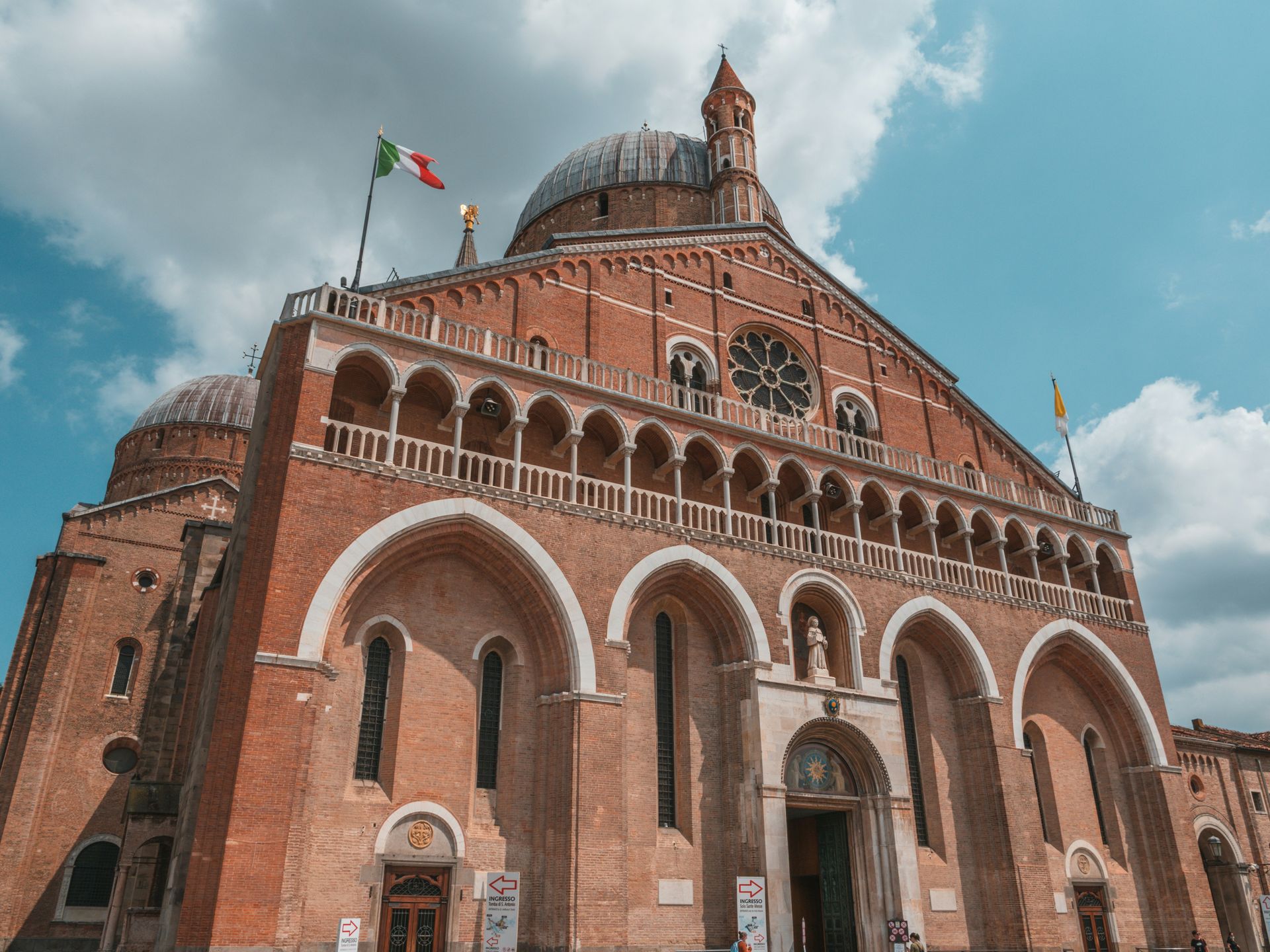 Basilika des Heiligen Antonius in Padua, Italien, rote Backsteinfassade, Bögen, Kuppel, italienische Flagge auf der Spitze.