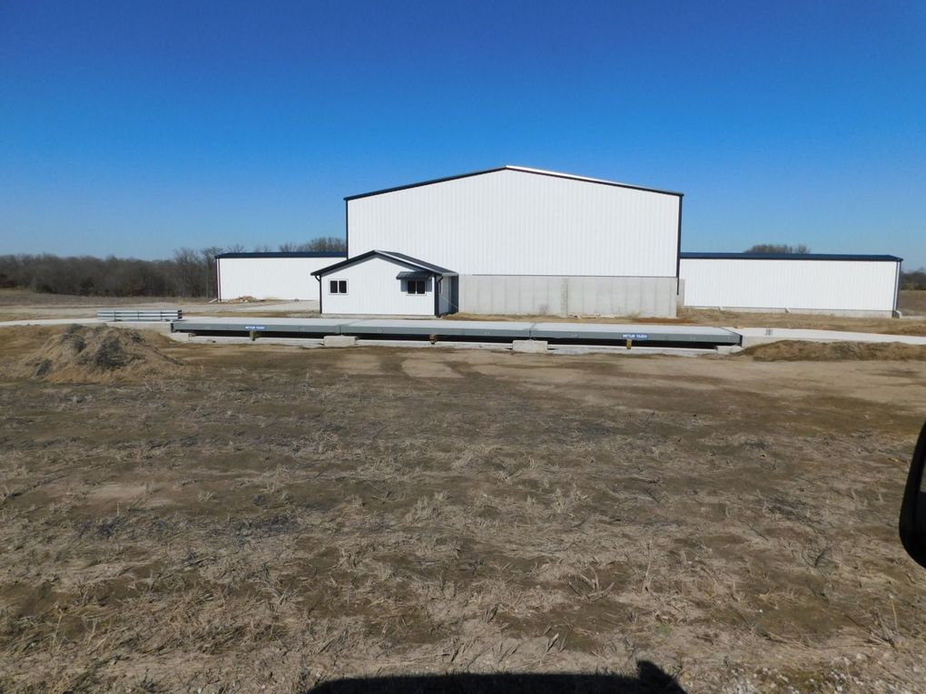 White industrial building with a small entrance, set on a barren lot under a clear blue sky.