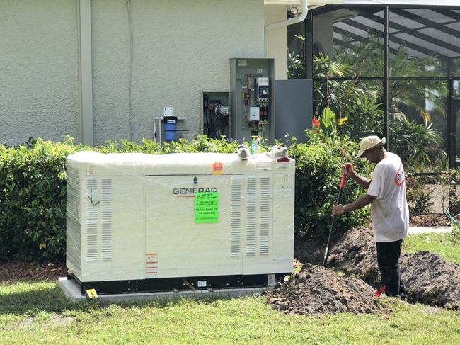 Man servicing a white generator in a yard. He's wearing a blue shirt and tan pants, working with tools.
