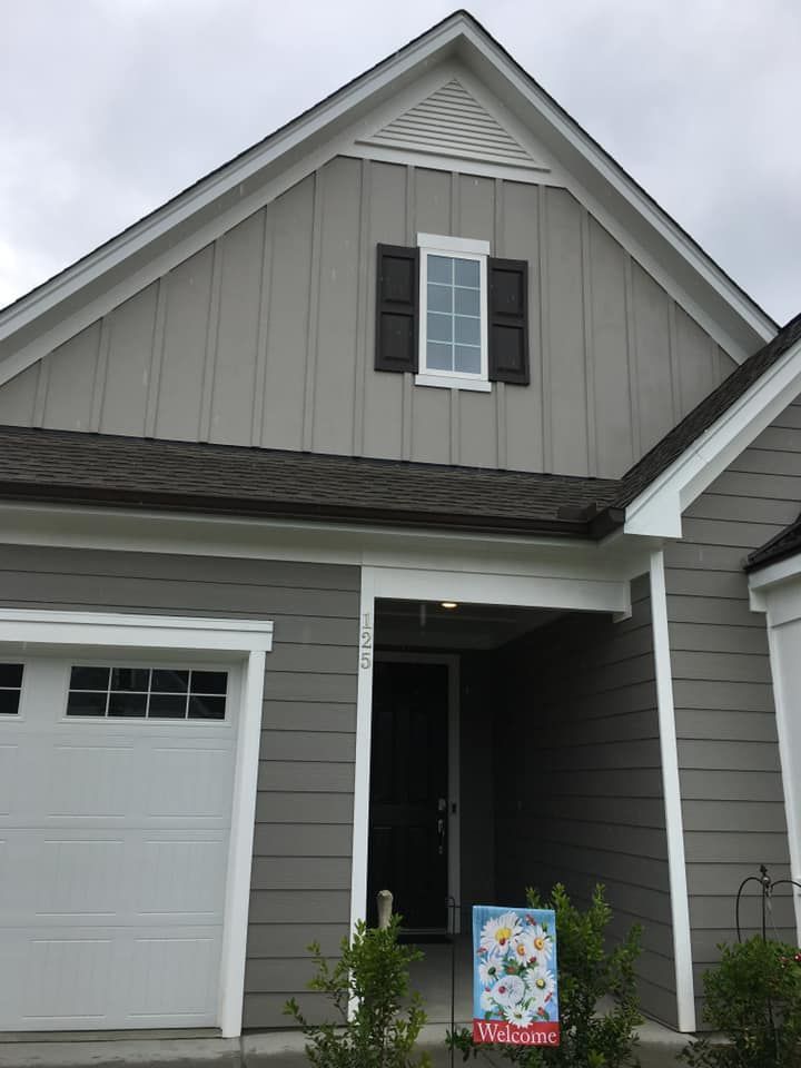 Gray townhouse exterior with white garage door, black shutters, and a colorful sign by the front porch