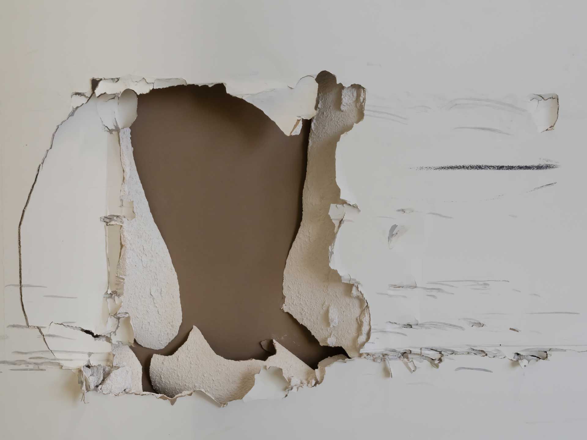 Large hole torn through a white wall, exposing brown drywall underneath.