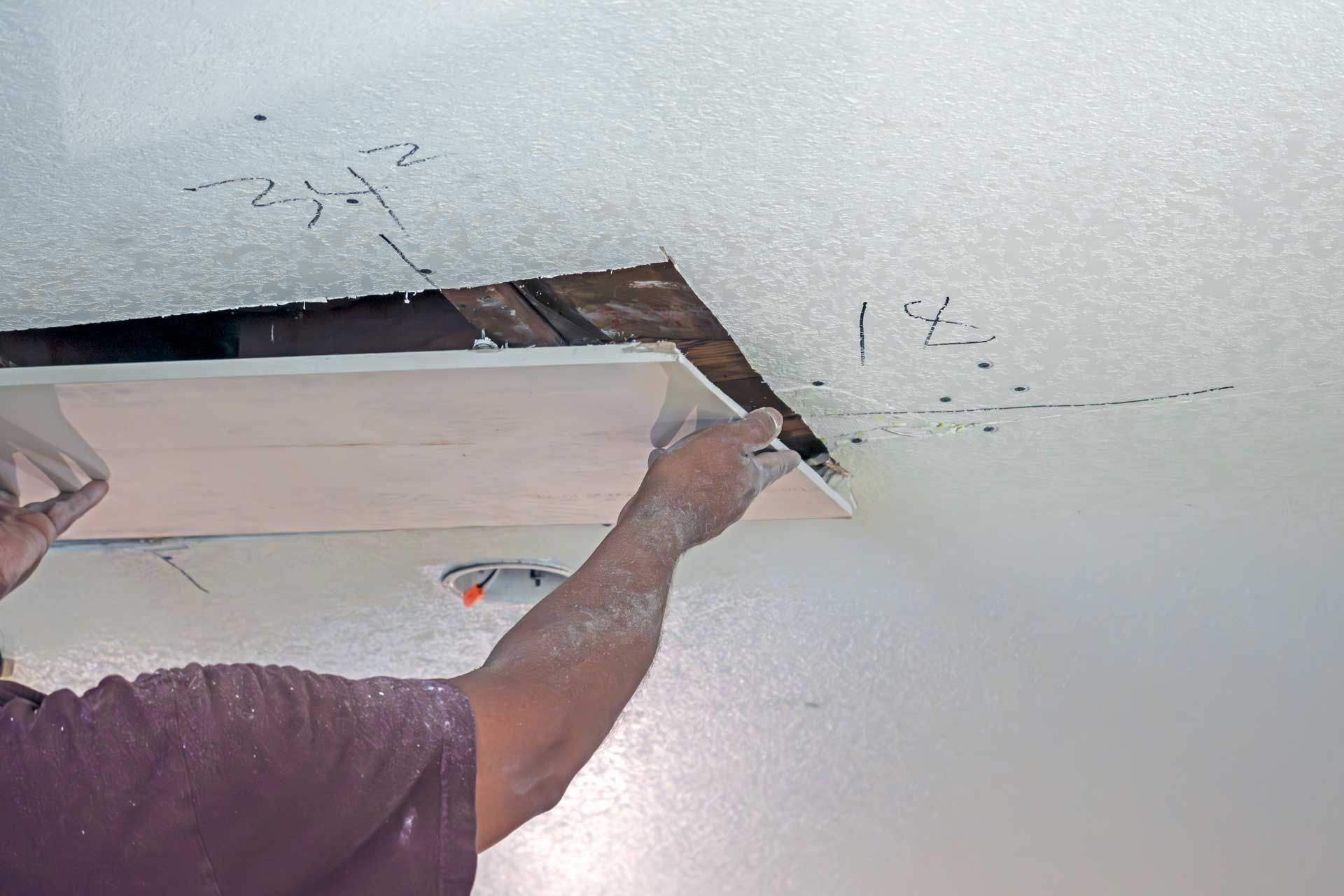 Person repairing a damaged ceiling, reaching up to patch a large hole with exposed wood.