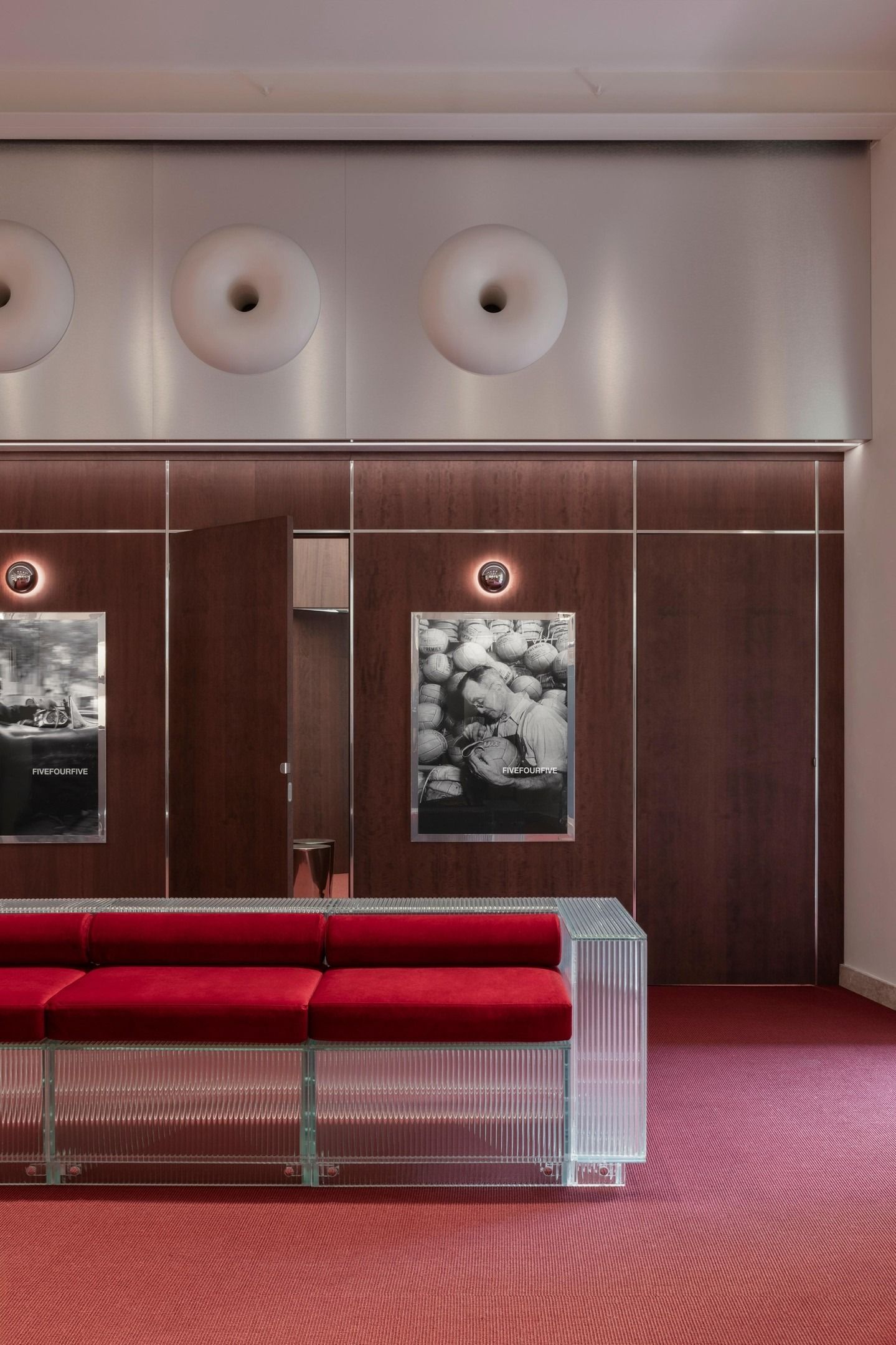 Atrio moderno con divano rosso, pareti rivestite in legno, quadri incorniciati e lampade circolari a soffitto.