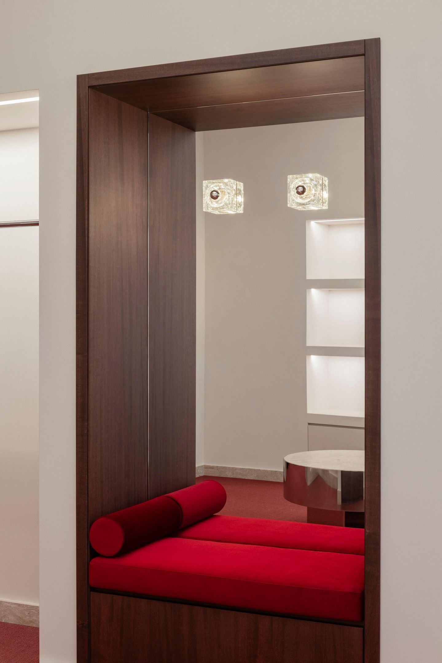 Panchina moderna rossa all'interno di una nicchia in legno con tavolino e applique a parete.