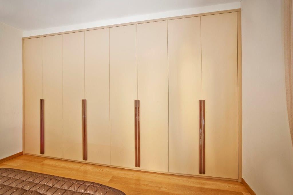 Parete di ante di armadio beige con maniglie verticali in legno.
