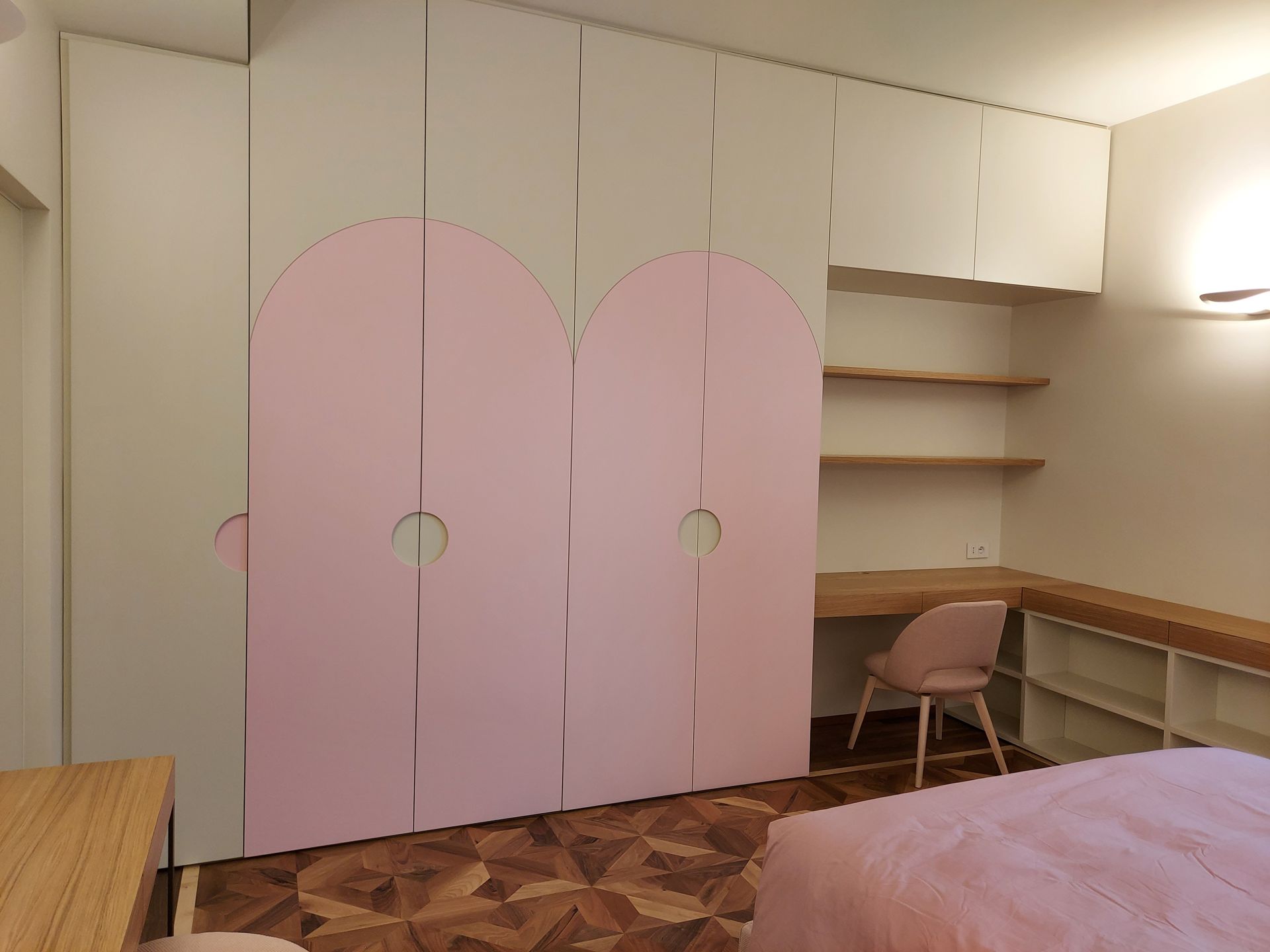 Ante dell'armadio rosa in una piccola camera da letto con scrivania, scaffali, sedia e letto.