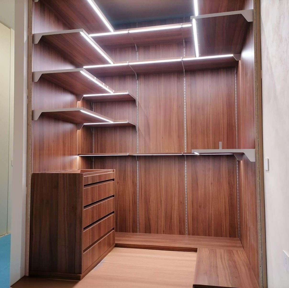 Cabina armadio vuota in legno con ripiani, cassetti e illuminazione a LED a luce calda.