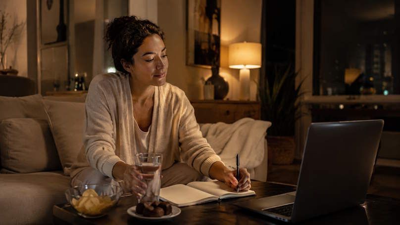 OKC woman at night sitting in her cozy living room drinking a glass of water instead of eating snacks supporting weight loss
