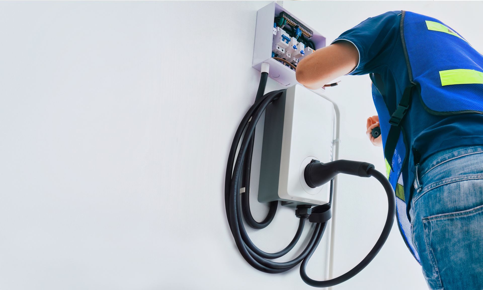 Technician wiring a wall-mounted EV charging station at an electrical panel. Technician wiring a wall-mounted EV charging station at an electrical panel.