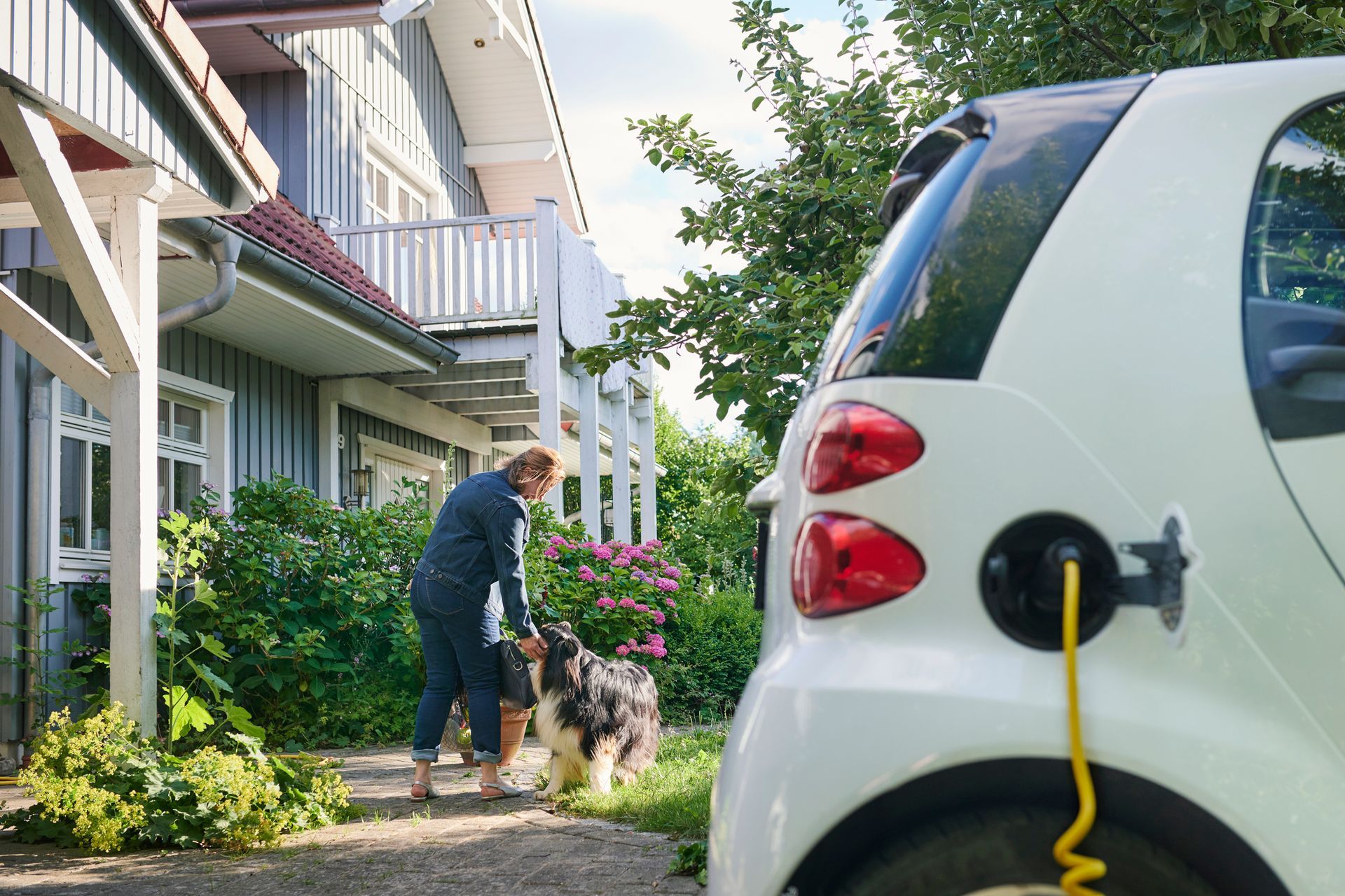 A woman walking to the entrance of her house while her electric car is charging