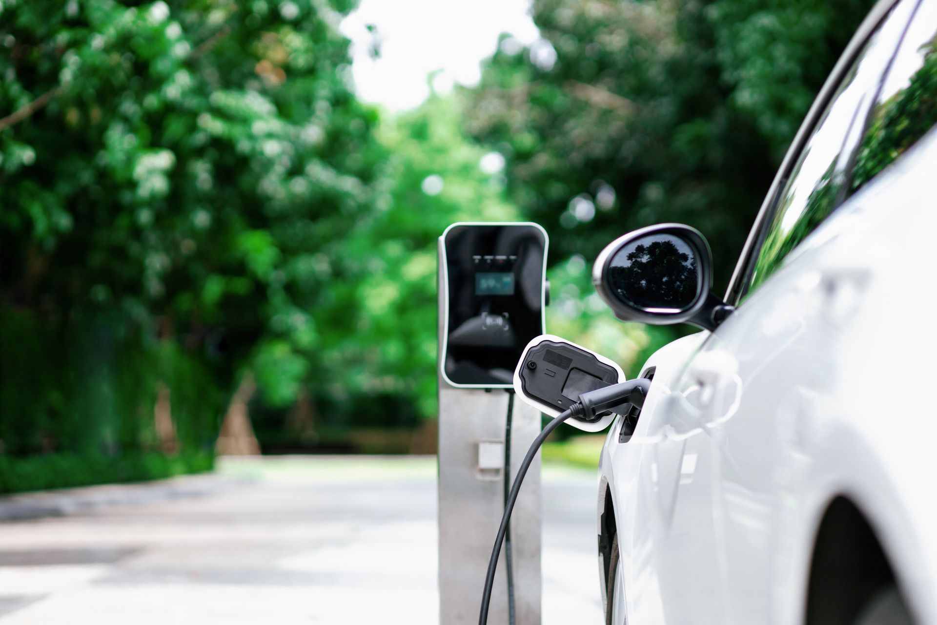 Close-up of an EV charging station installed at a home, charging a white car.