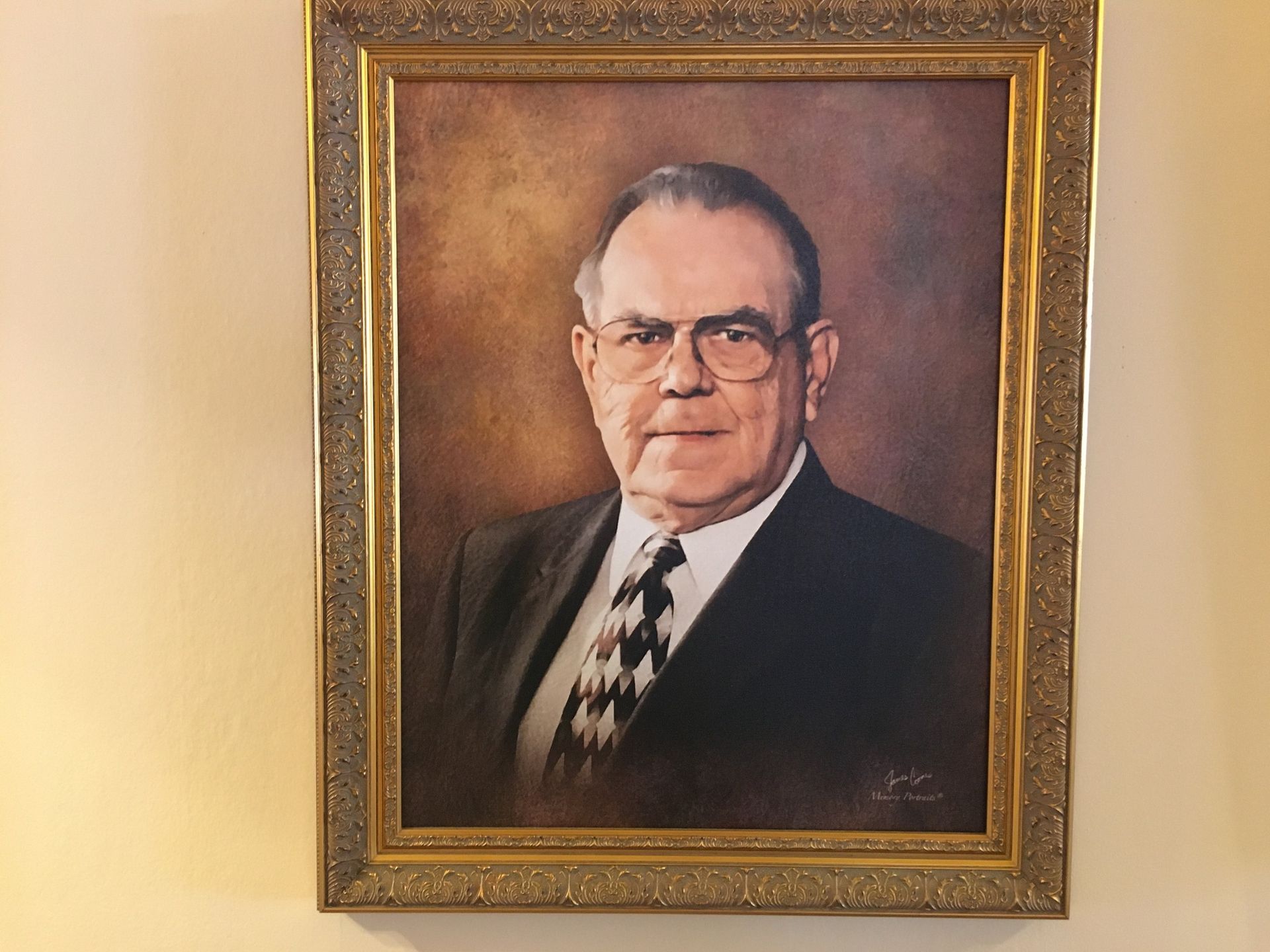 Framed portrait of a man in a suit and tie hanging on a beige wall.