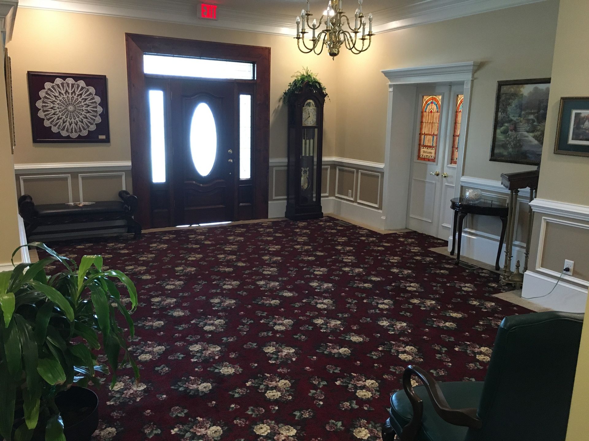 Elegant lobby with red patterned carpet, double front doors, wall art, and chandeliers