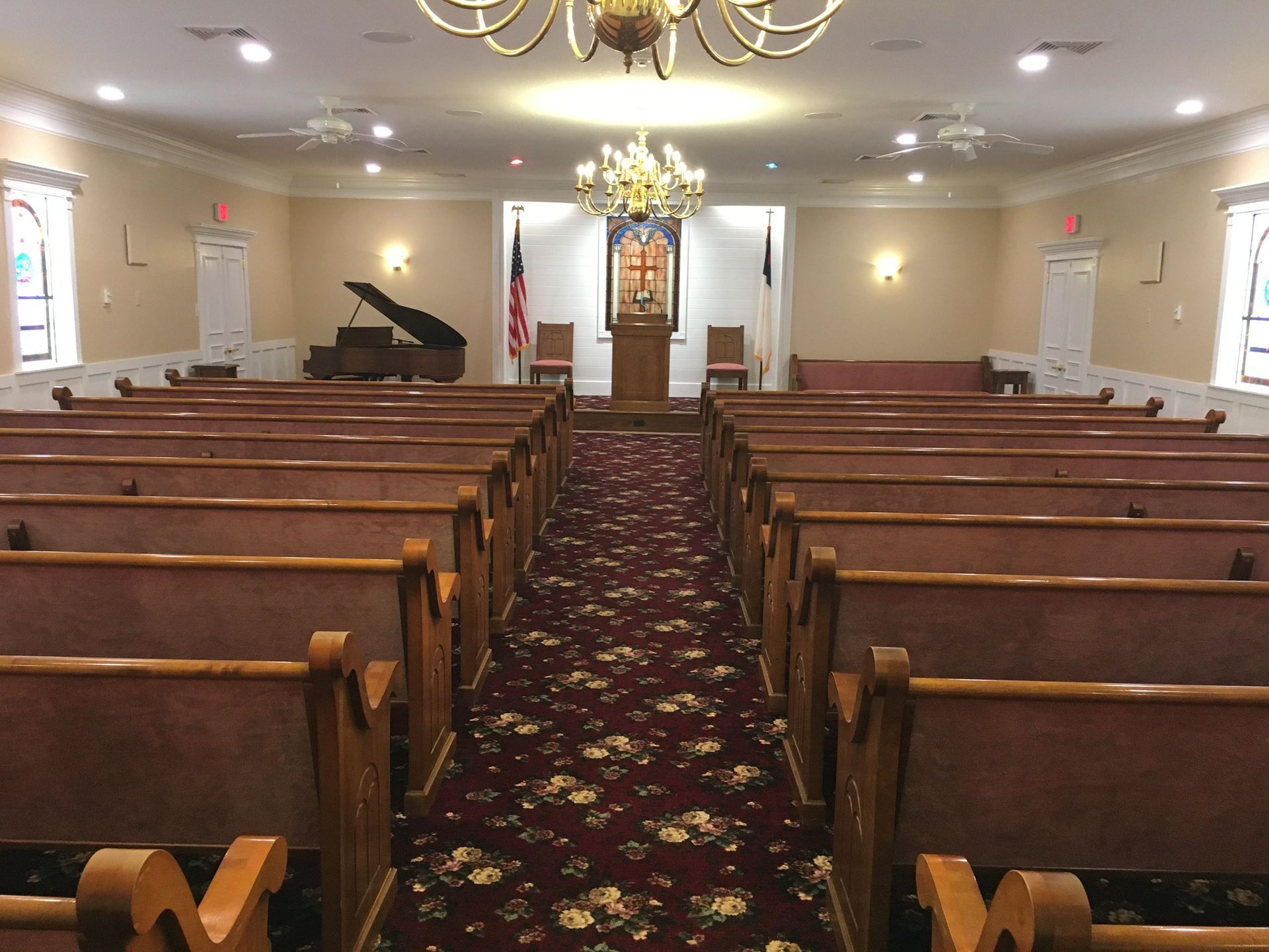 Empty church sanctuary with wooden pews, floral carpet, and piano near the front altar.